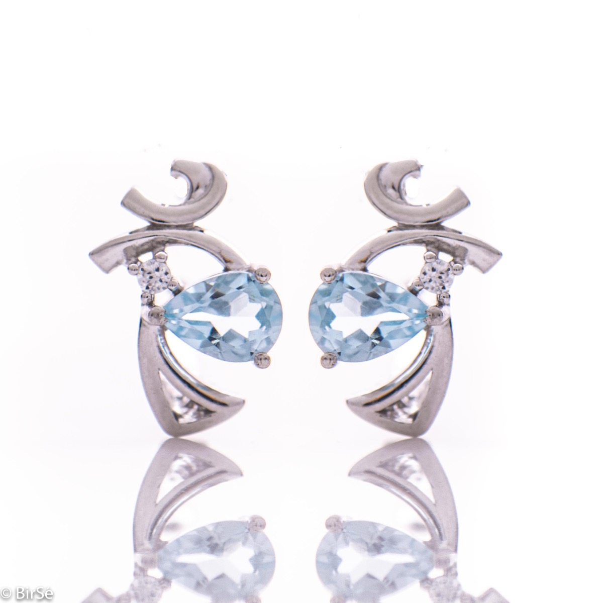 Delicate English clasp earrings for women featuring a radiant natural blue topaz stone, in a delicate teardrop shape, surrounded by graceful curves of rhodium silver and a fine cubic zirconia finish. In an exclusive pendant and ring set.