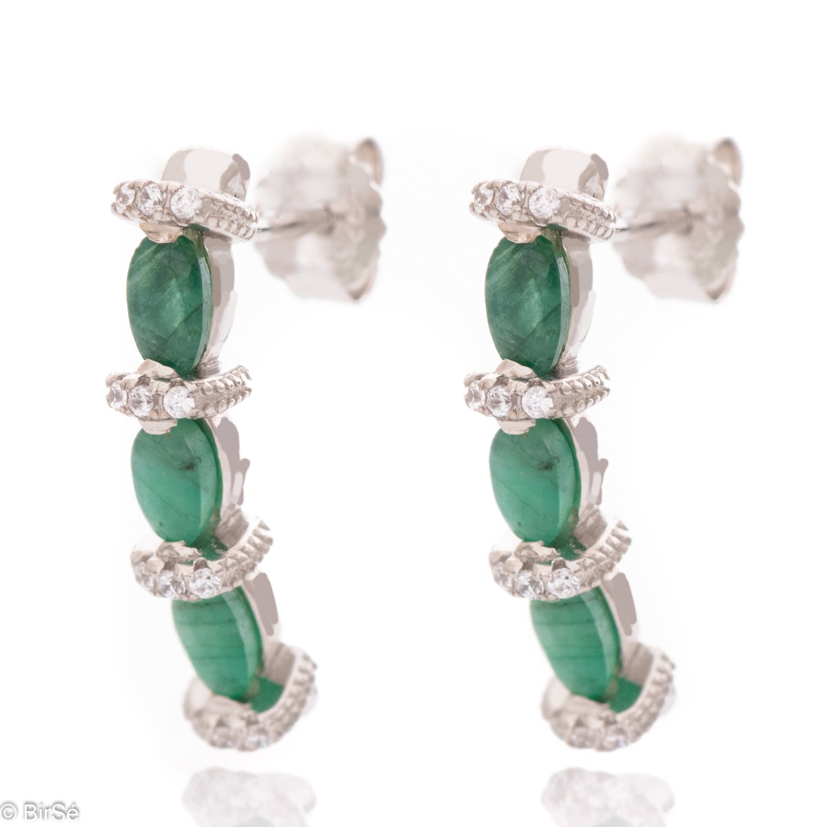 Elegant earrings made of rhodium silver and a magnificent emerald, delicately combined with zircons. A stylish design, successfully applied in a pendant and ring by the model.