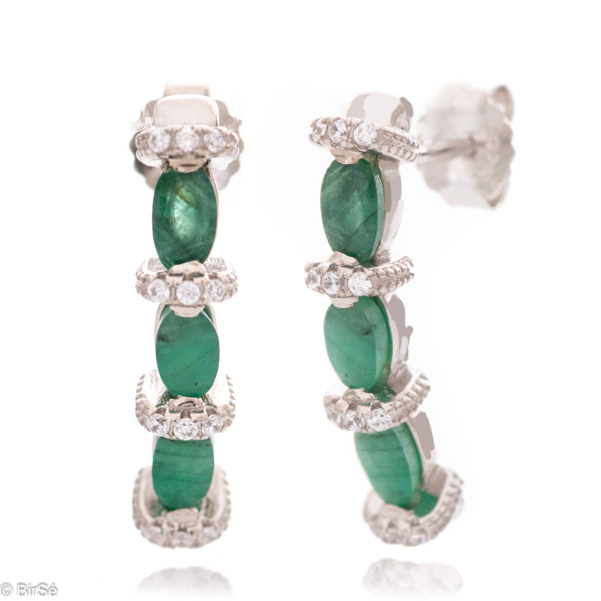 Elegant earrings made of rhodium silver and a magnificent emerald, delicately combined with zircons. A stylish design, successfully applied in a pendant and ring by the model.