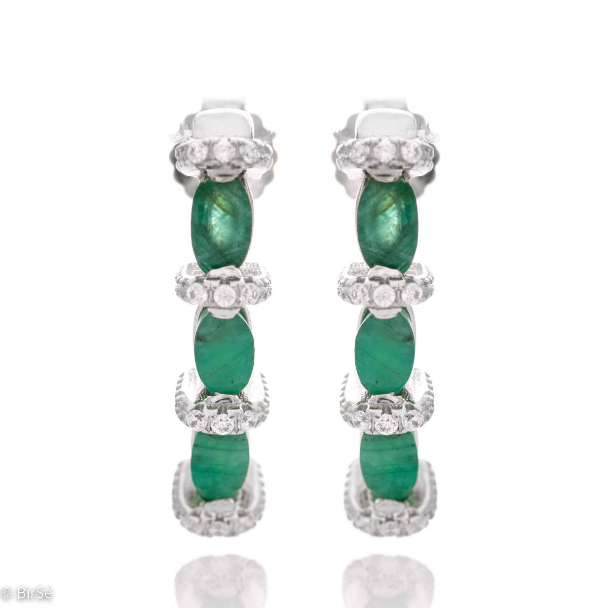 Elegant earrings made of rhodium silver and a magnificent emerald, delicately combined with zircons. A stylish design, successfully applied in a pendant and ring by the model.