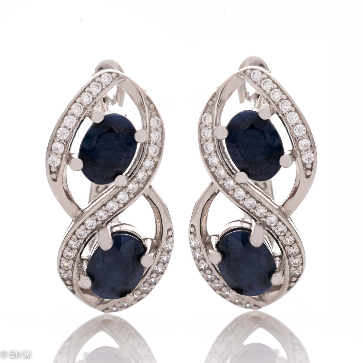 Stunning earrings beautifully crafted in rhodium-plated sterling silver with an infinity shape, exquisitely embellished with sparkling cubic zirconias surrounding magnetic sapphires. Complete with a ring of the same design.