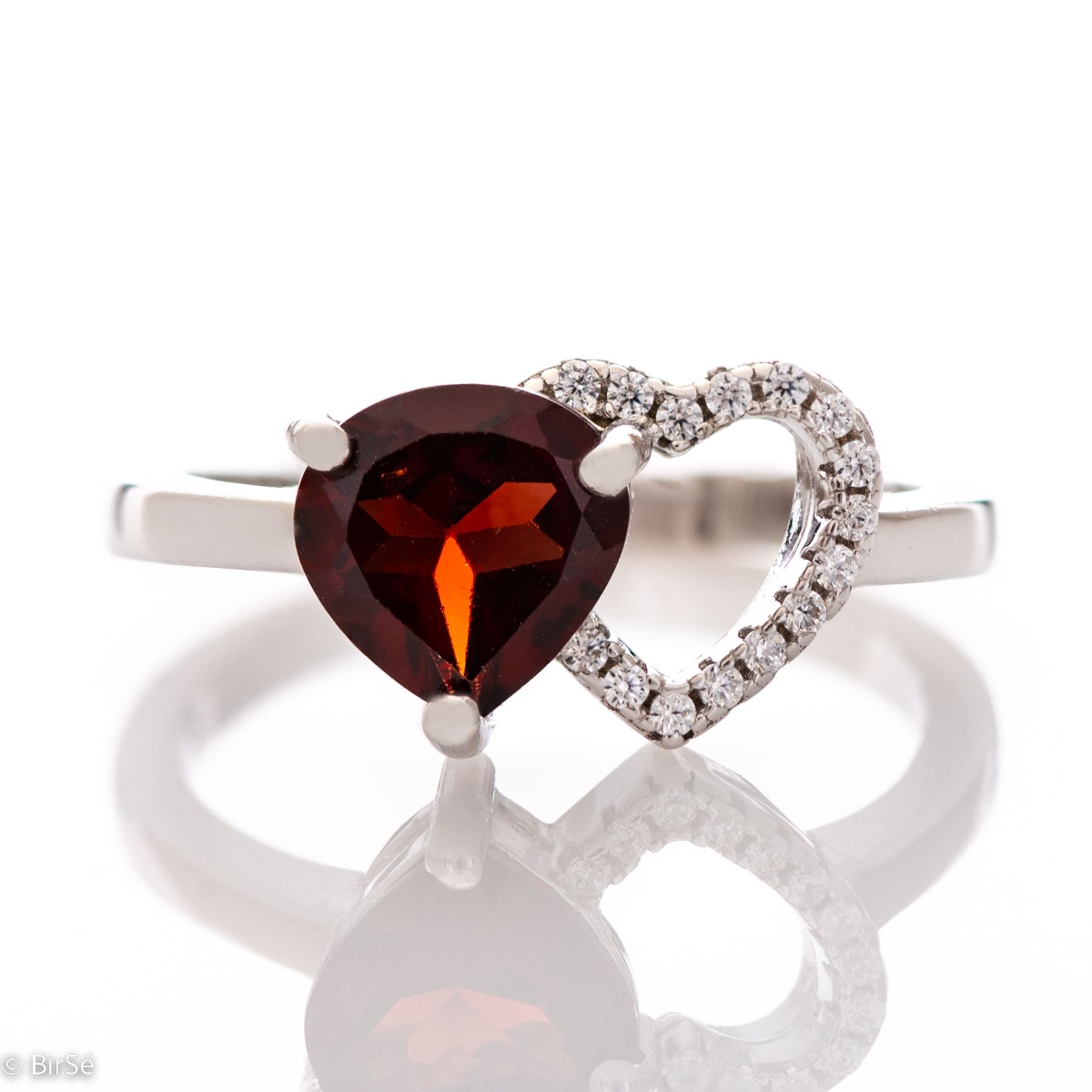 A spectacular ring made of a fine combination of rhodium-plated silver and stunning cubic zirconia stones, elegantly covering a beautiful heart. An enchanted natural garnet stone is gently nestled against the heart. The jewel is part of a set of dangling 