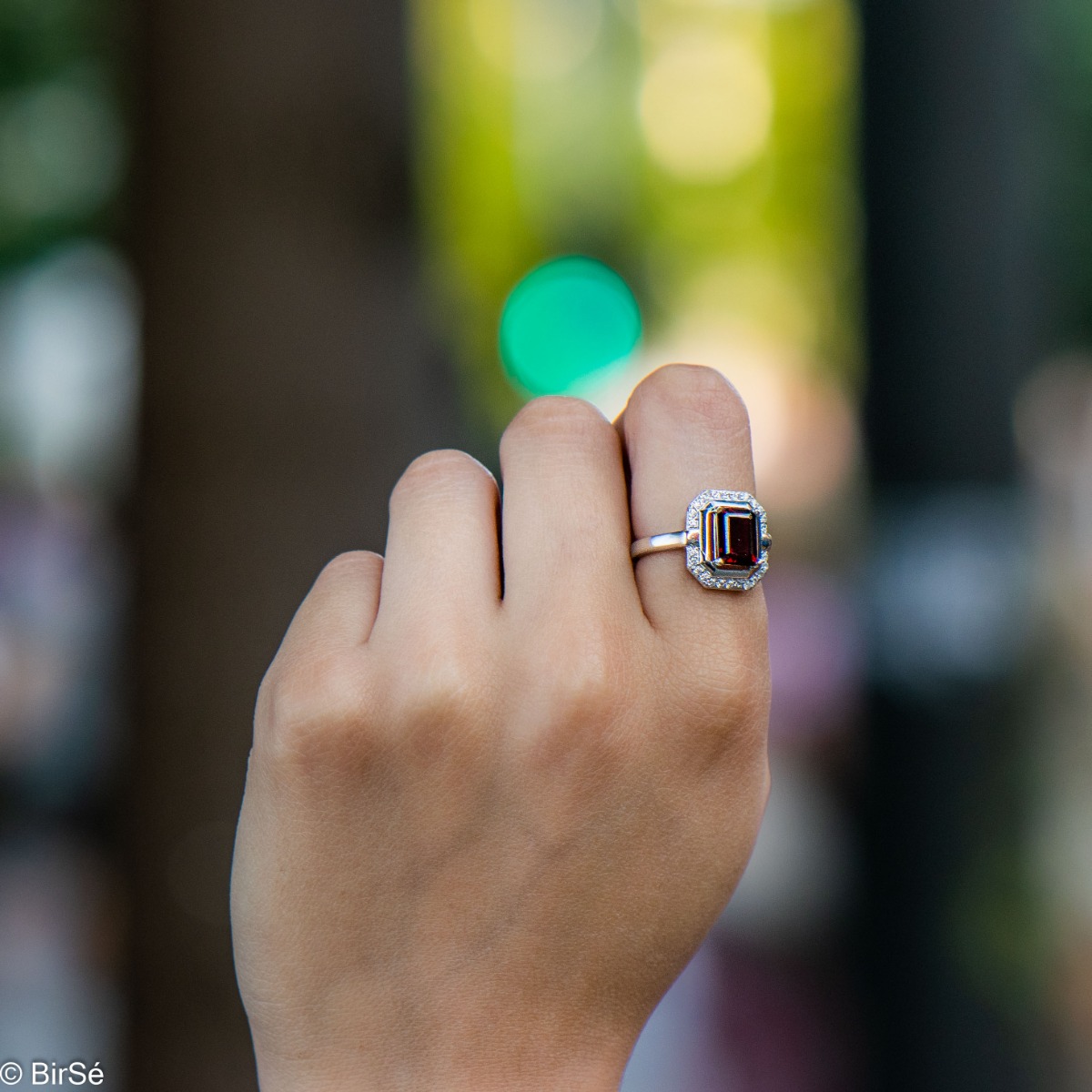 An elegant women's ring made of rhodium-plated silver, combined with the gentle glow of a natural garnet stone, surrounded by sparkling zircons. It can be combined with a pendant and earrings of the same model.