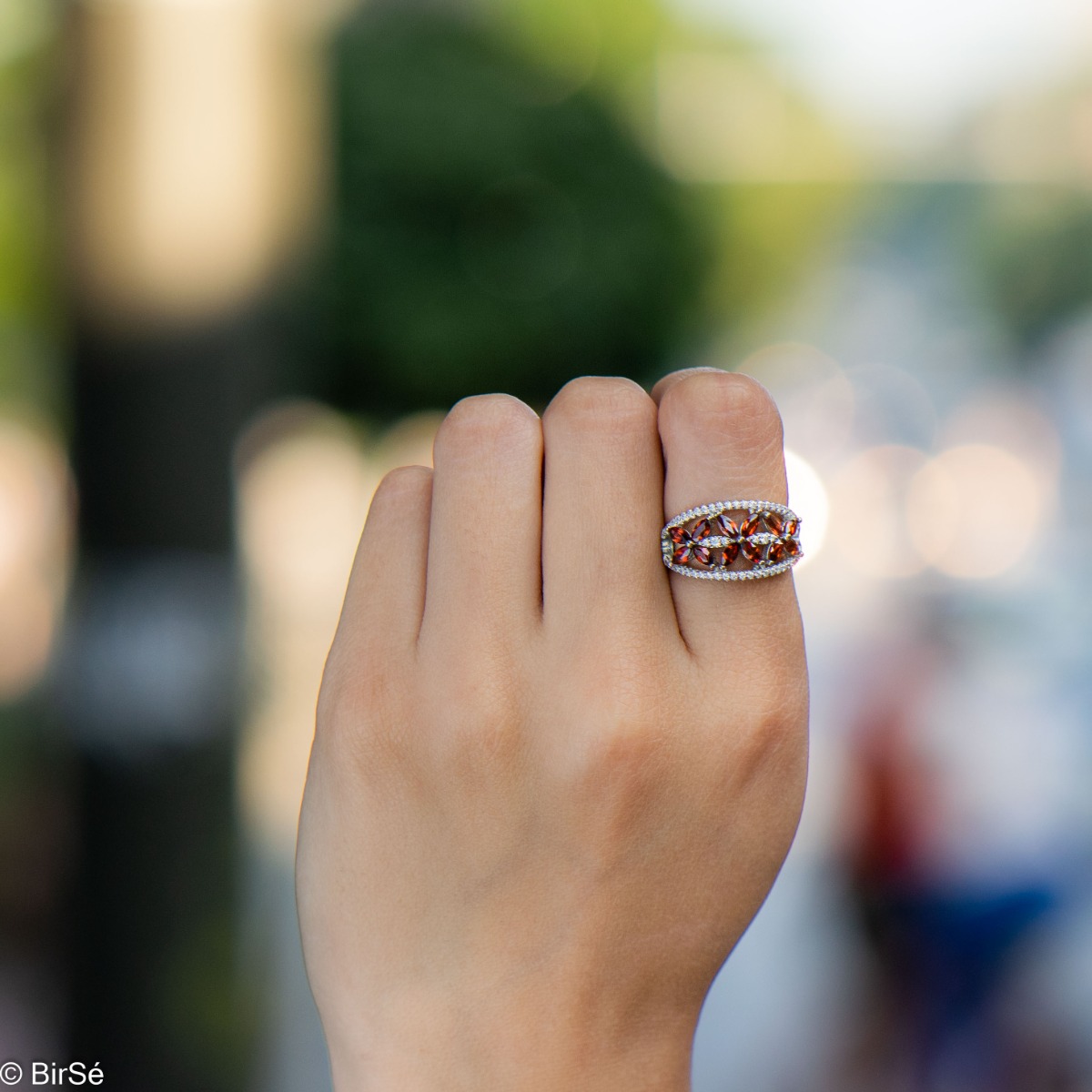 An elegant women's ring with a spectacular design entirely of rhodium-plated silver, combined with delicate flowers of natural garnet and zircons. Can be combined with earrings and pendant of the same model.