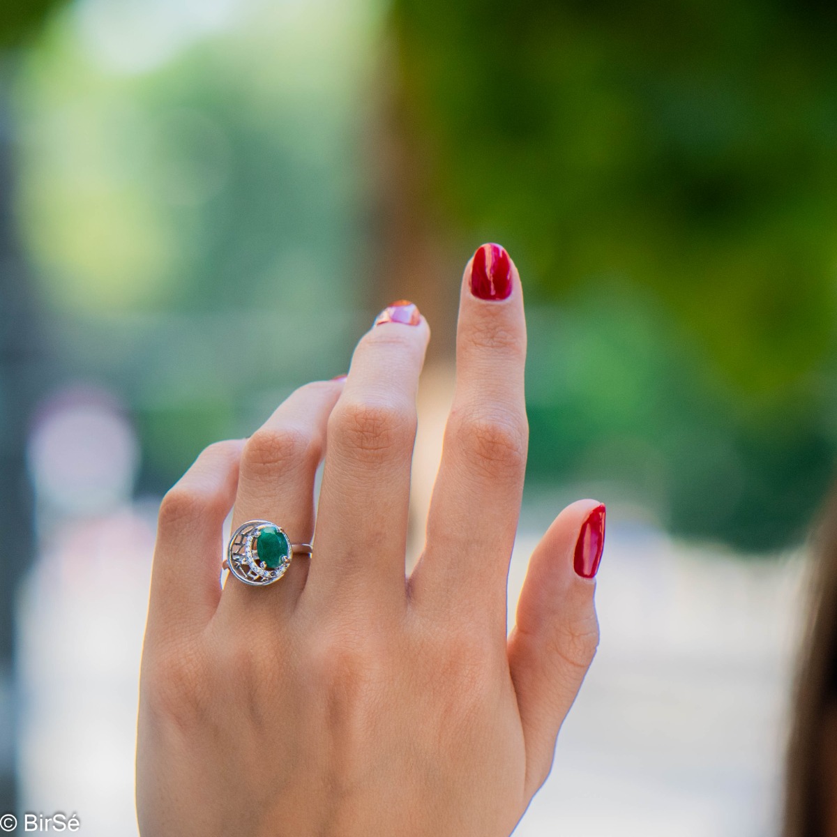 An elegant women's ring with ethereally shaped details, made entirely of rhodium-plated silver in combination with exquisite zircon stones and a captivating emerald.