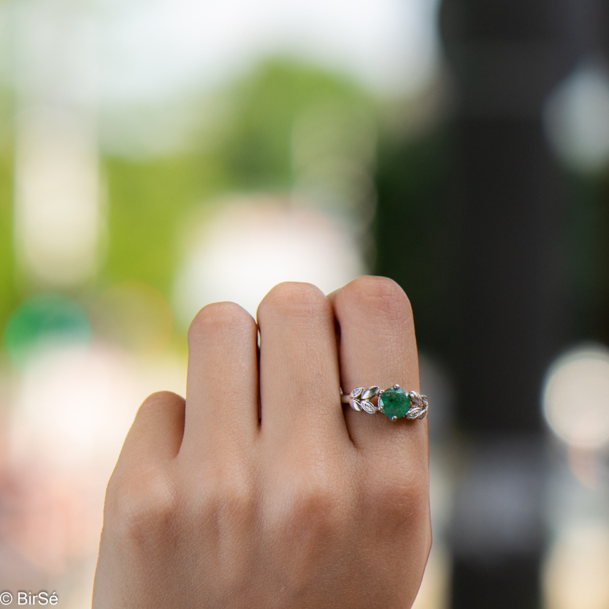 An elegant women's ring with delicate craftsmanship combining refined rhodium-plated silver with a radiant natural emerald and petals of sparkling zircons. Can be combined with earrings and pendant of the same model.