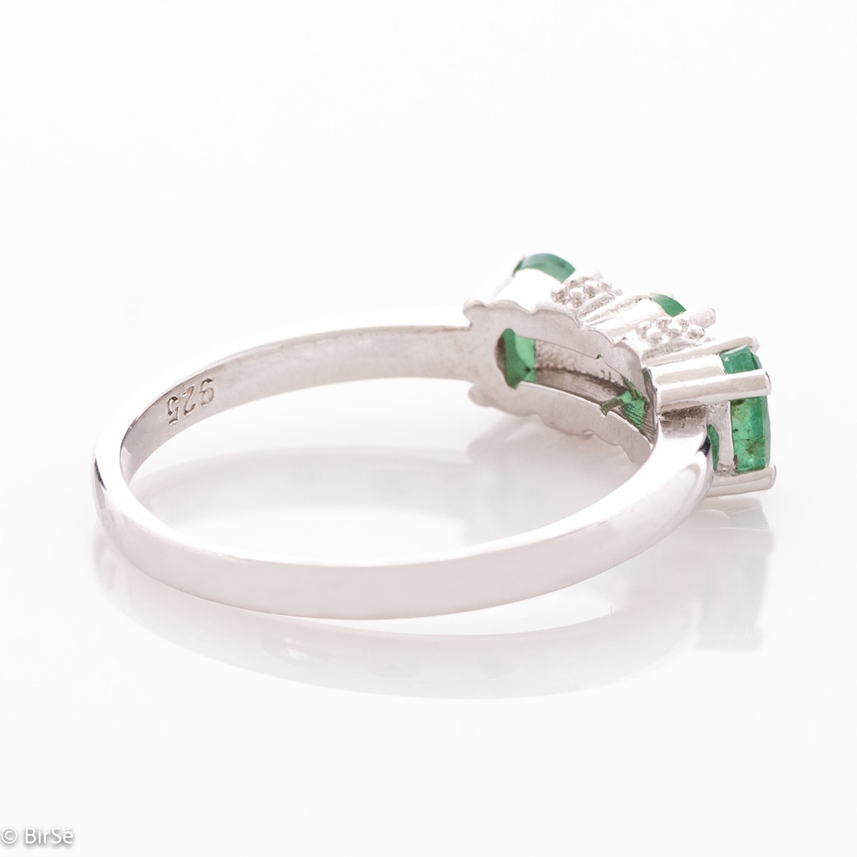 An elegant women's ring with delicate craftsmanship combining rhodium-plated silver with three brilliant natural emerald stones and sparkling zircons.