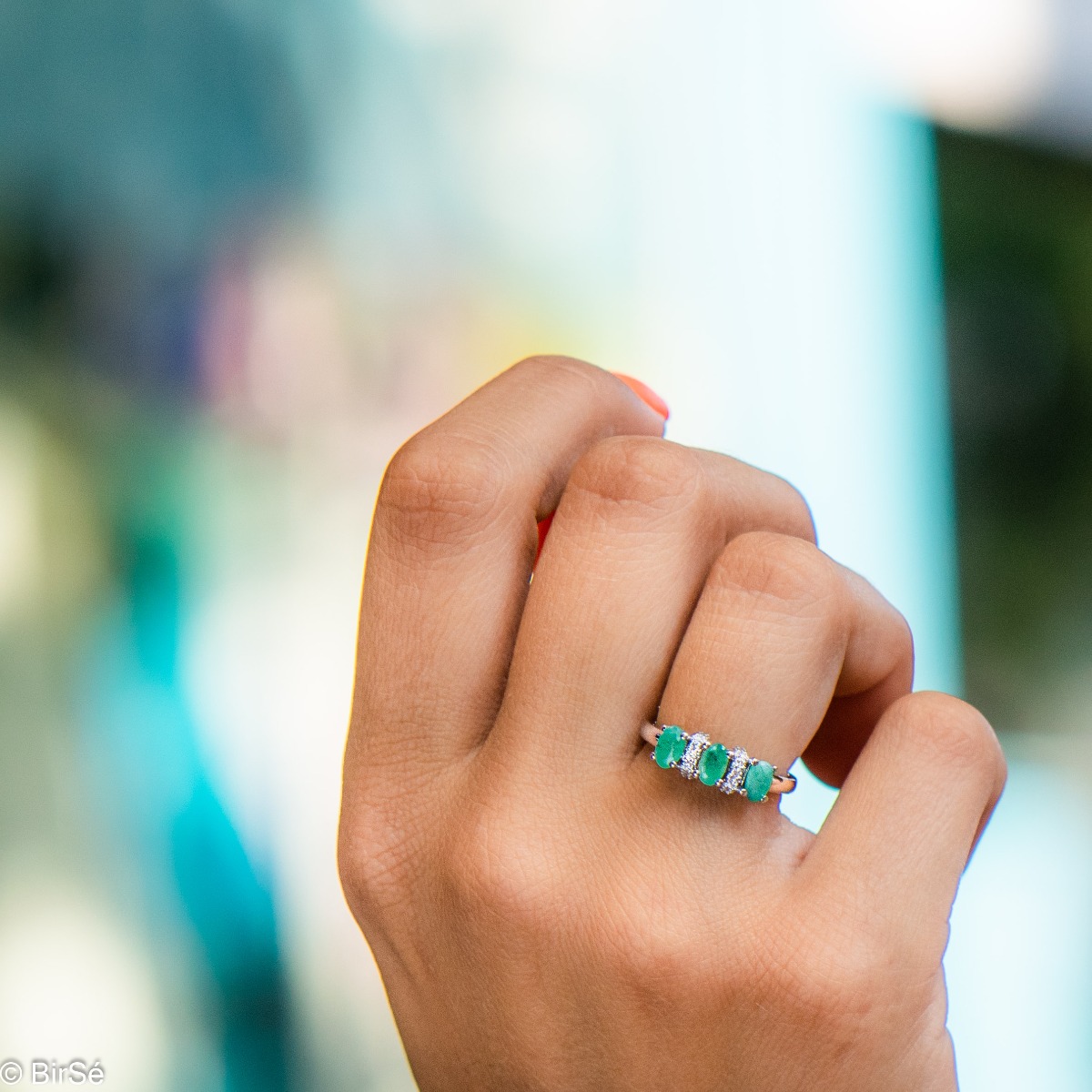 An elegant women's ring with delicate craftsmanship combining rhodium-plated silver with three brilliant natural emerald stones and sparkling zircons.