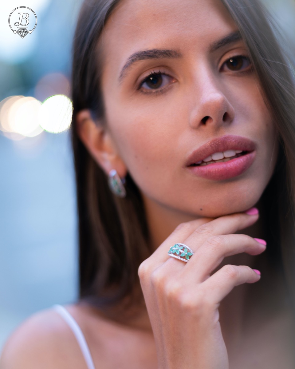 An elegant women's ring with a spectacular workmanship entirely of rhodium-plated silver, combined with delicate flowers of natural emerald and zircons. Can be combined with earrings and pendant of the same model.