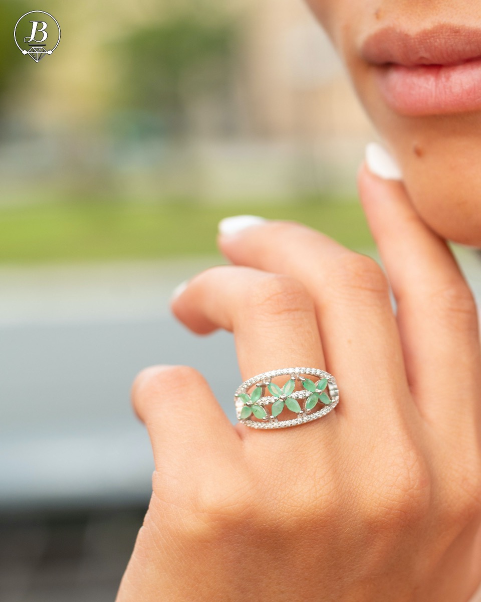 An elegant women's ring with a spectacular workmanship entirely of rhodium-plated silver, combined with delicate flowers of natural emerald and zircons. Can be combined with earrings and pendant of the same model.