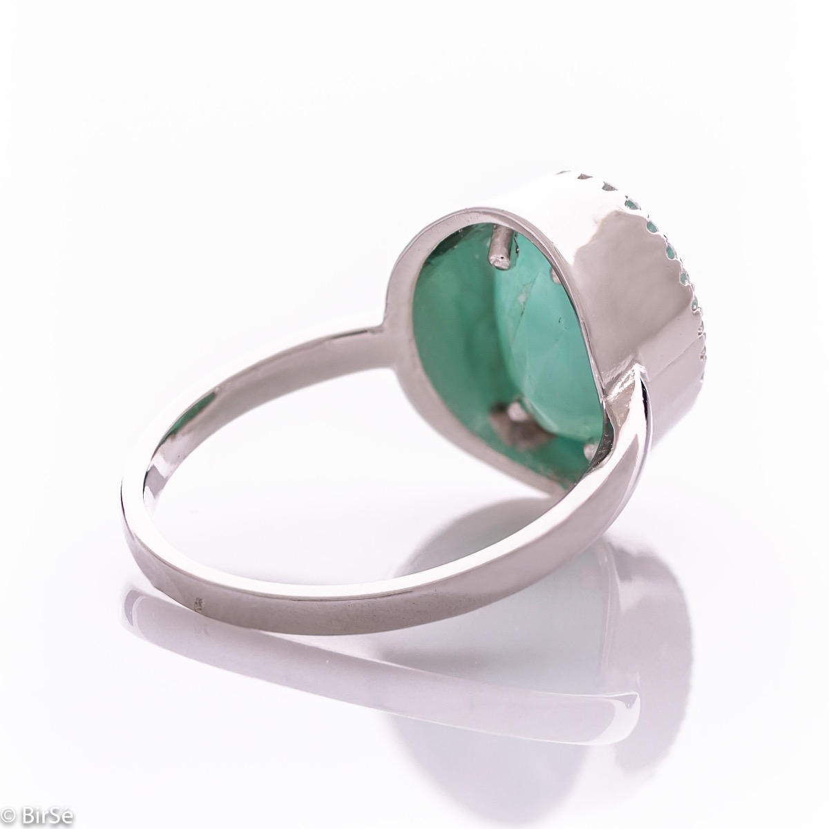 An elegant women's ring with precise craftsmanship combining a radiant natural emerald surrounded by sparkling zircons and delicate rhodium silver. It can be combined with a pendant and earrings of the same model.