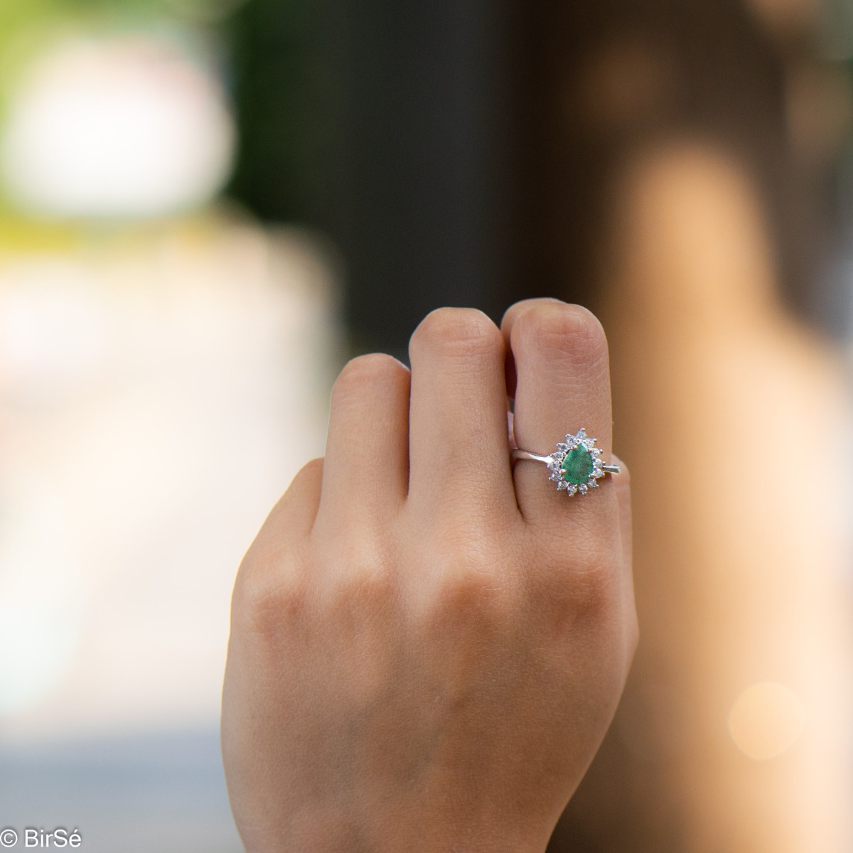 Delicate women's ring with a radiant natural emerald stone, in a beautiful teardrop shape, surrounded by sparkling zircons and made entirely of rhodium-plated silver.