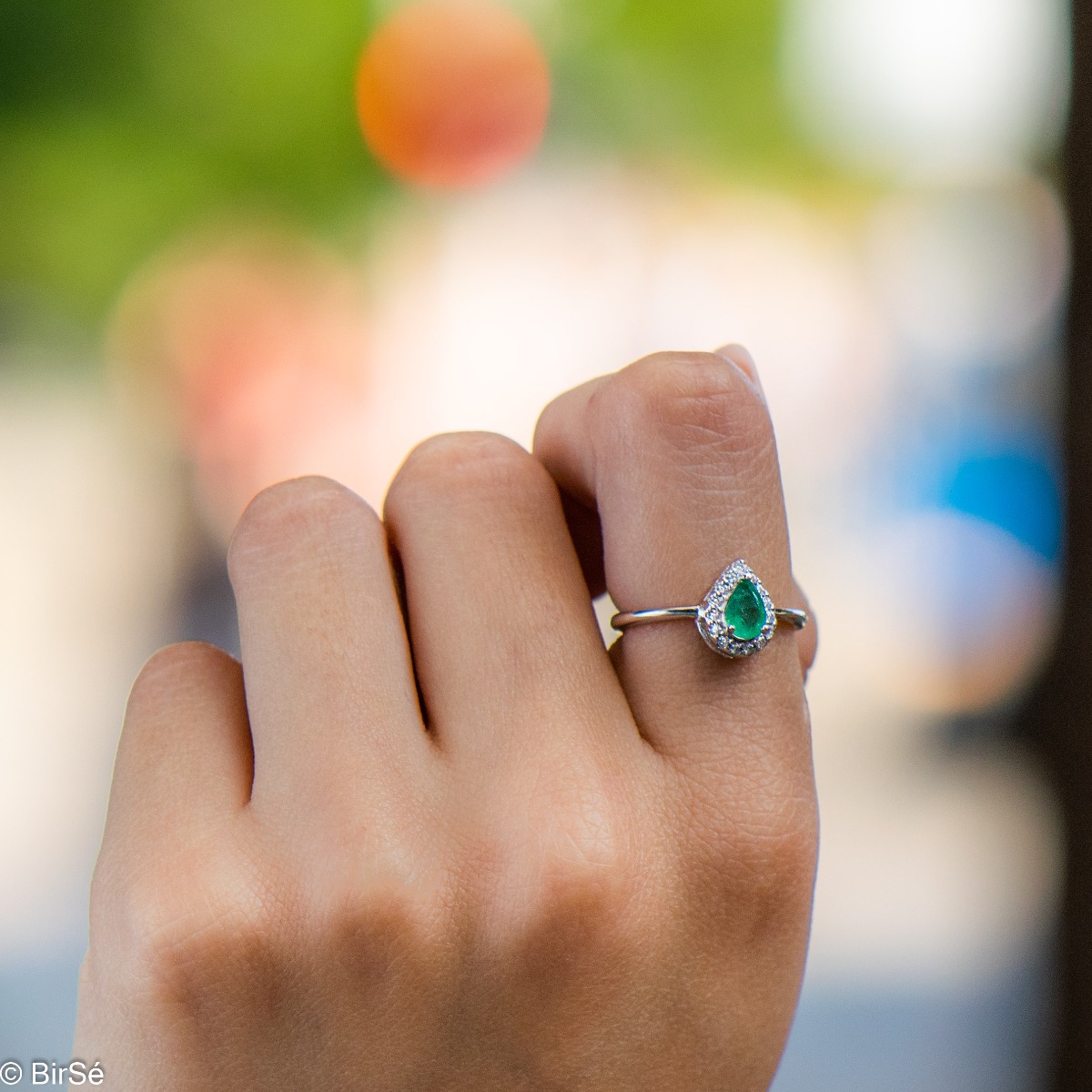 Delicate women's ring with an exquisite natural emerald stone, with a beautiful teardrop shape, surrounded by sparkling zircons and made entirely of rhodium-plated silver.