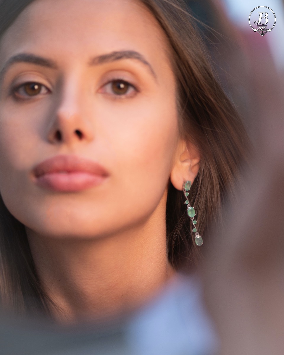 Extremely impressive dangling earrings with delicate workmanship combining numerous natural emerald stones with shiny rhodium silver.