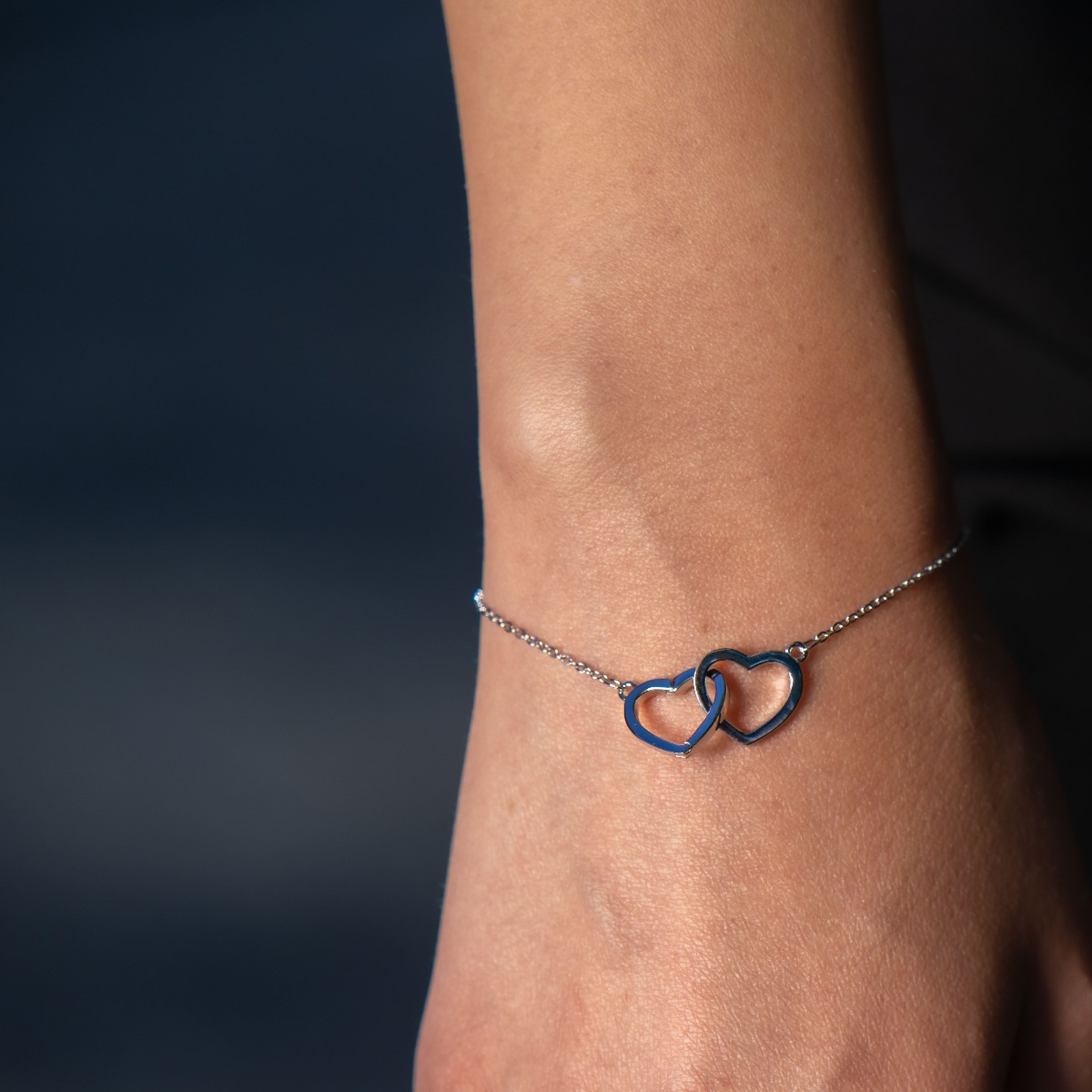 An elegant women's bracelet with delicate workmanship entirely of shiny rhodium-plated silver and two beautiful, intertwined hearts. Stylish and clean composition of details and adjustable size, suitable for all ladies.