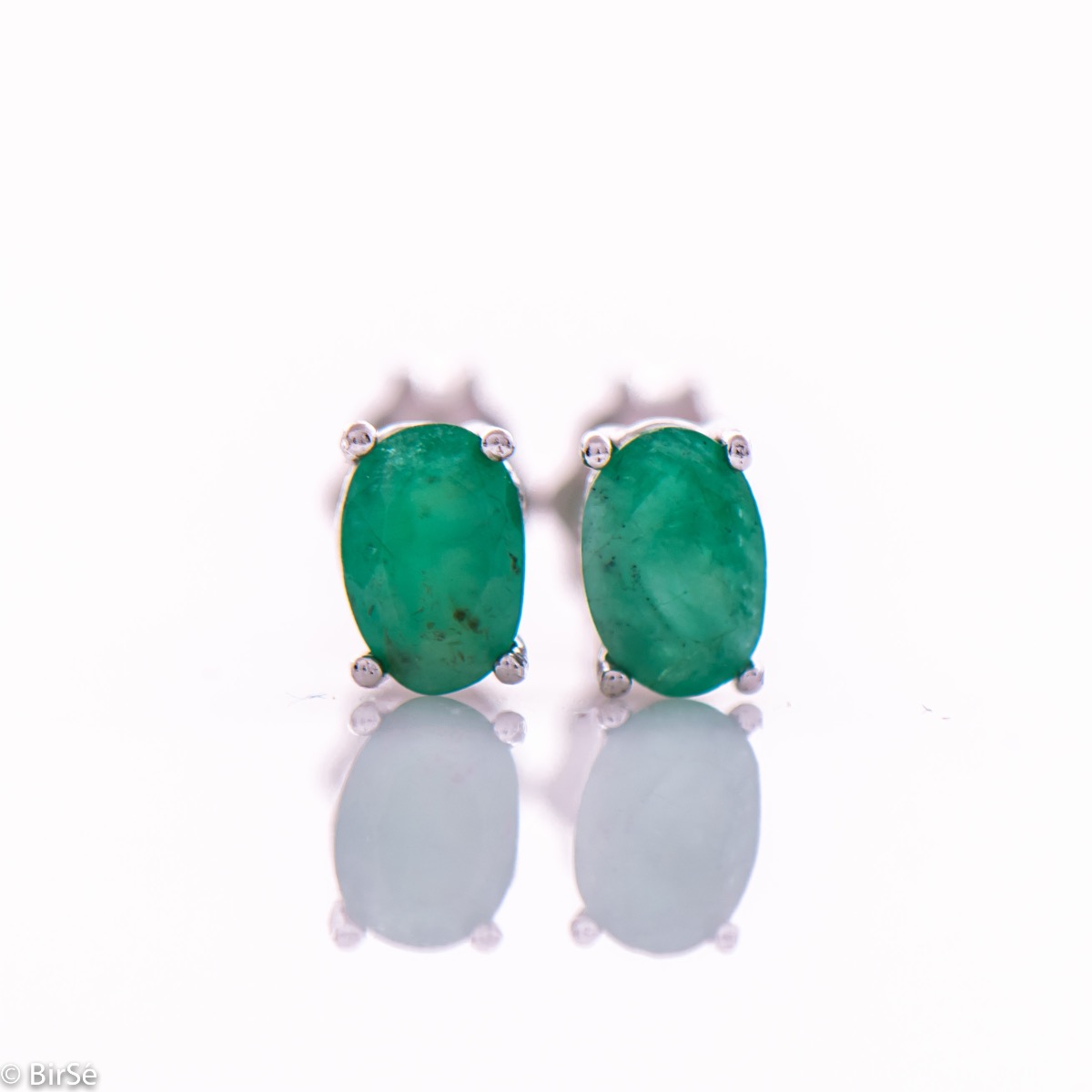 Elegant women's stud earrings with a clean design and a gentle combination of shiny rhodium silver with a radiant natural emerald stone in an elegant oval shape.