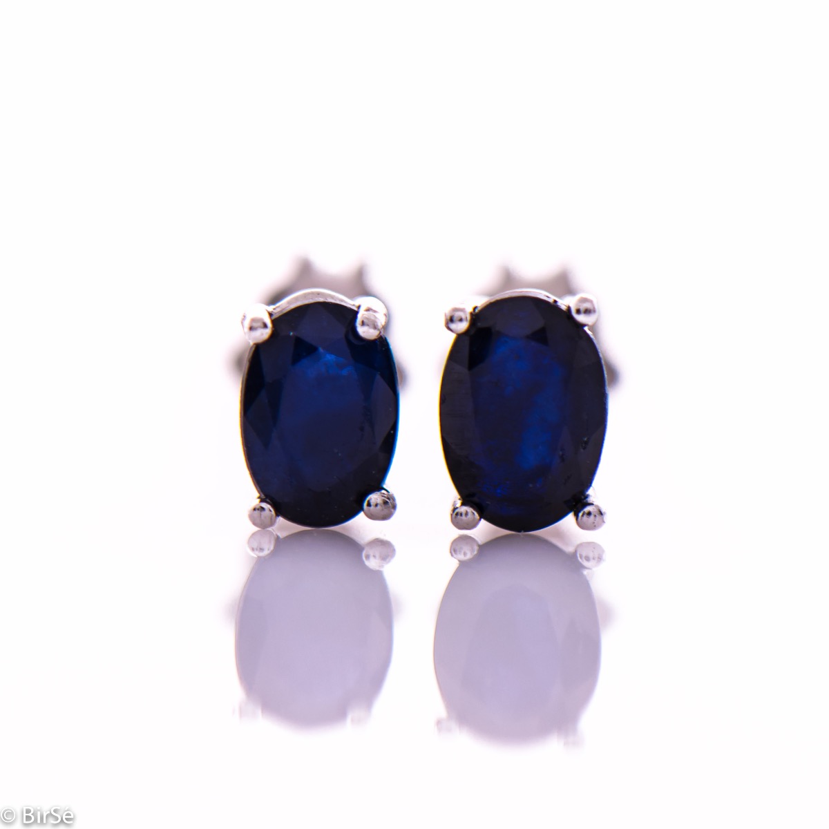 Elegant women's stud earrings with a clean design and a gentle combination of shiny rhodium silver with a radiant natural sapphire stone in an elegant oval shape.