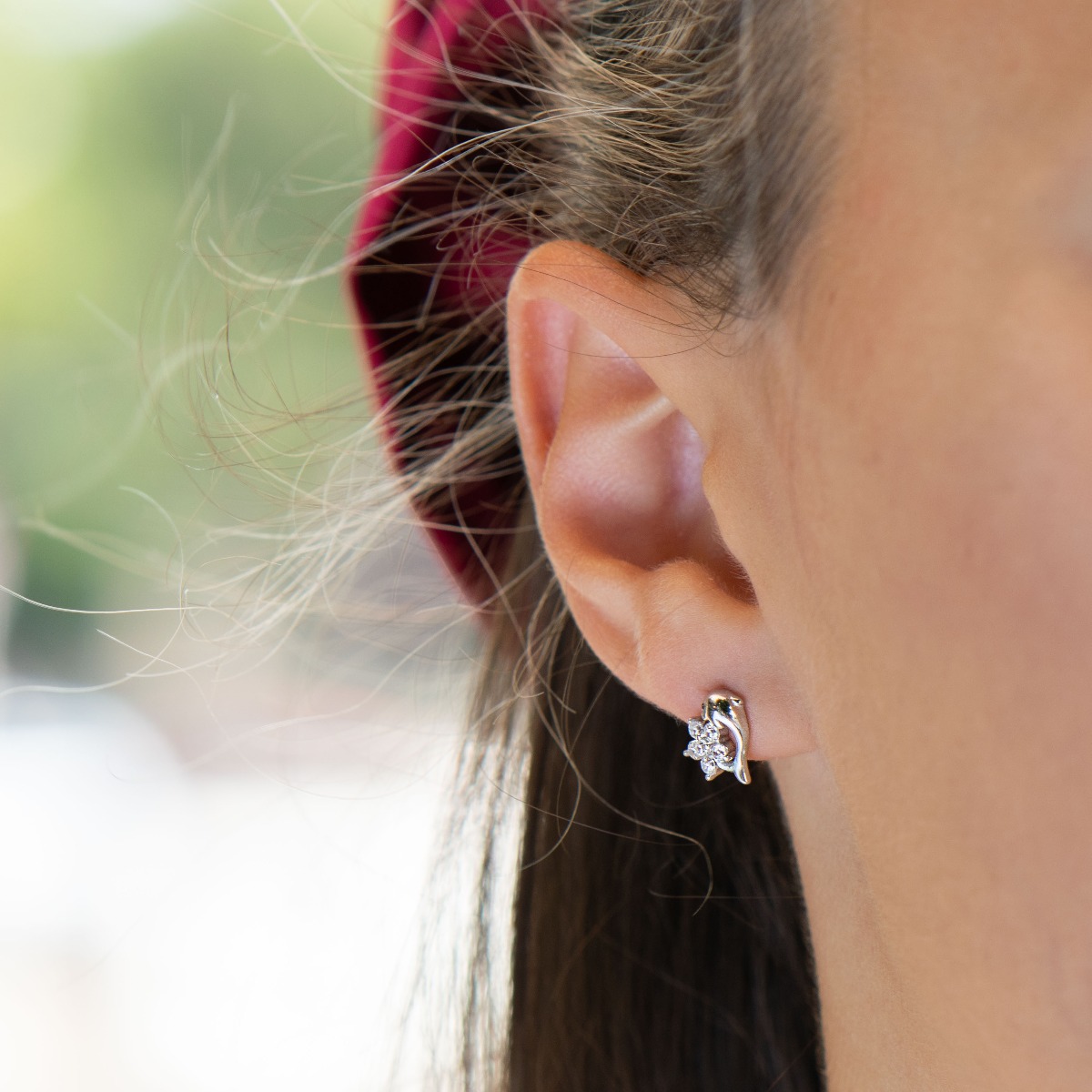 Delicate women's earrings in fine rhodium silver, with an interesting design layout of a charming dolphin, embracing a flower of sparkling zircons.