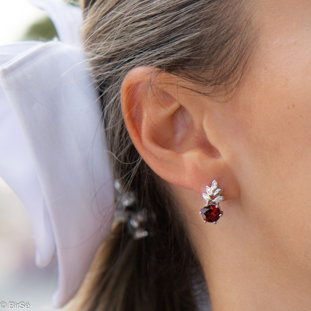 Delicate ladies' earrings with an English clasp and an exclusive design combining a radiant natural garnet surrounded by petals of zircons and made entirely of rhodium-plated silver. They can be combined with a pendant and a ring of the same model.