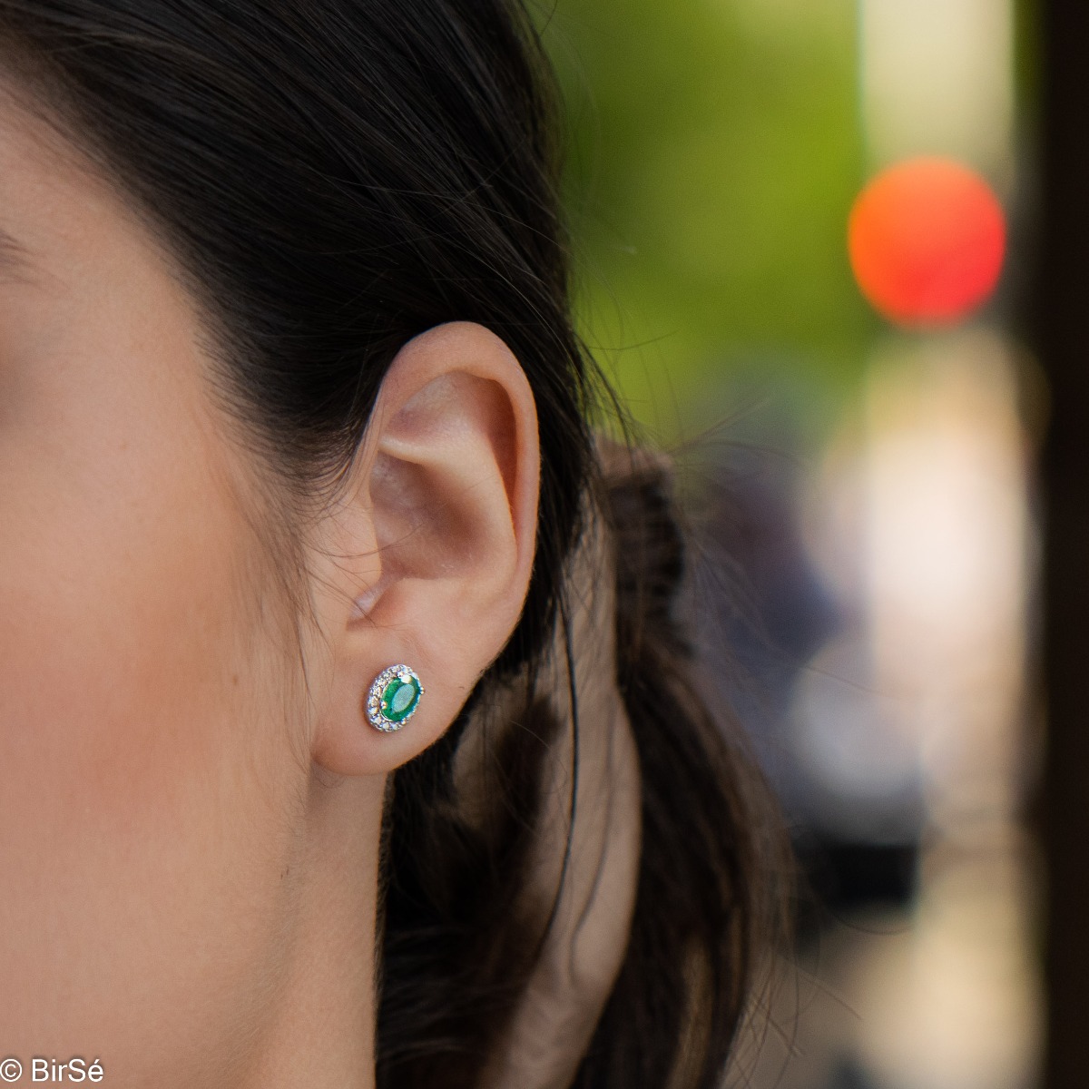 Stylish women's earrings with an elegantly shaped pattern of rhodium-plated silver and a natural emerald stone, beautifully surrounded by dazzling zircons.