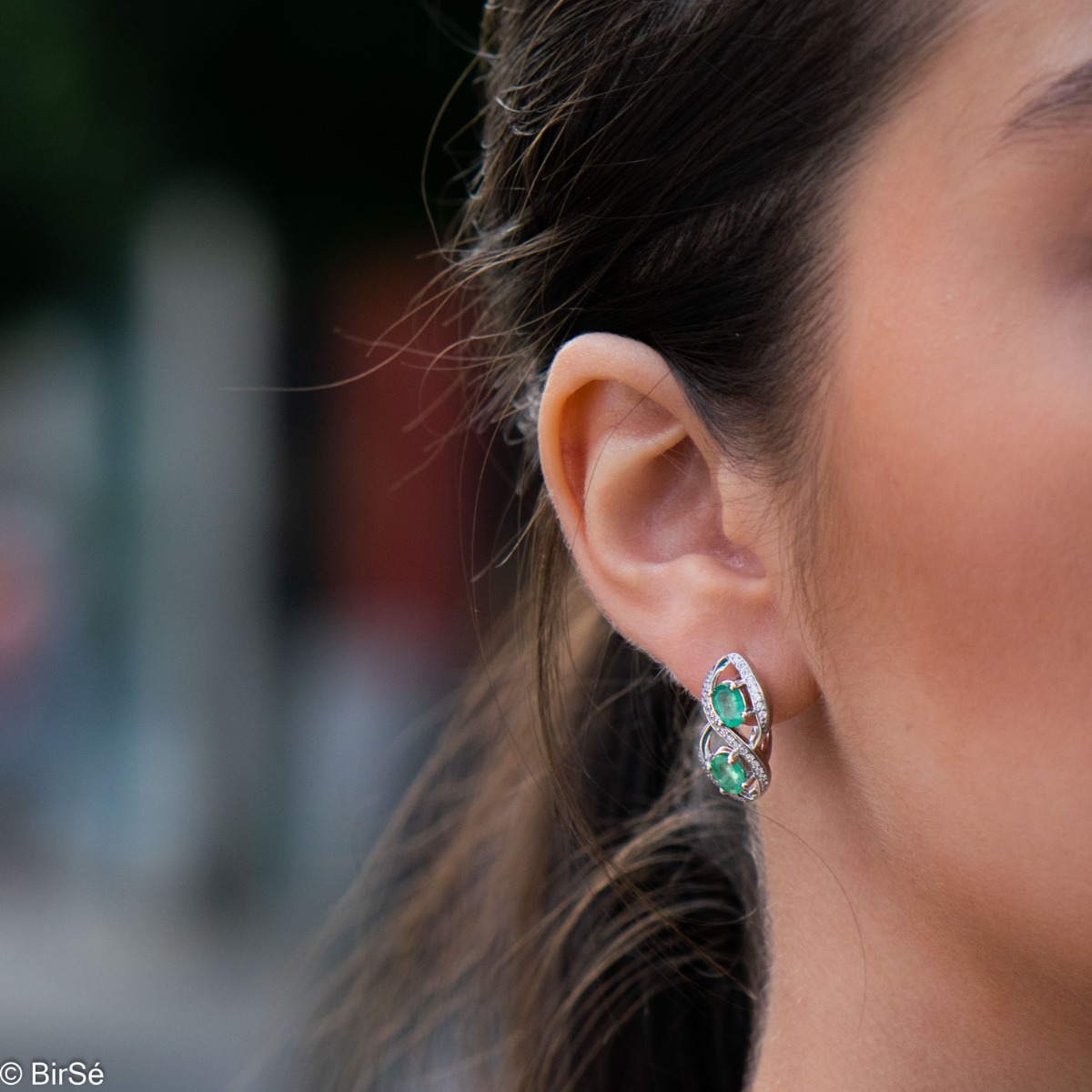 Stunning infinity rhodium-plated sterling silver earrings, exquisitely embellished with glittering cubic zirconias encircling gorgeous emeralds. Complete with a ring of the same design.