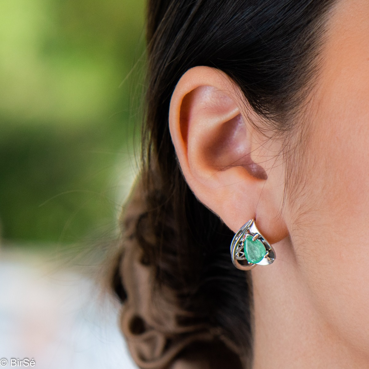 Captivating women's earrings with English clasp and beautiful curves and details crafted from soft rhodium-plated sterling silver, complemented by a radiant natural emerald stone in an exquisite teardrop shape. In a charming pendant and ring set.