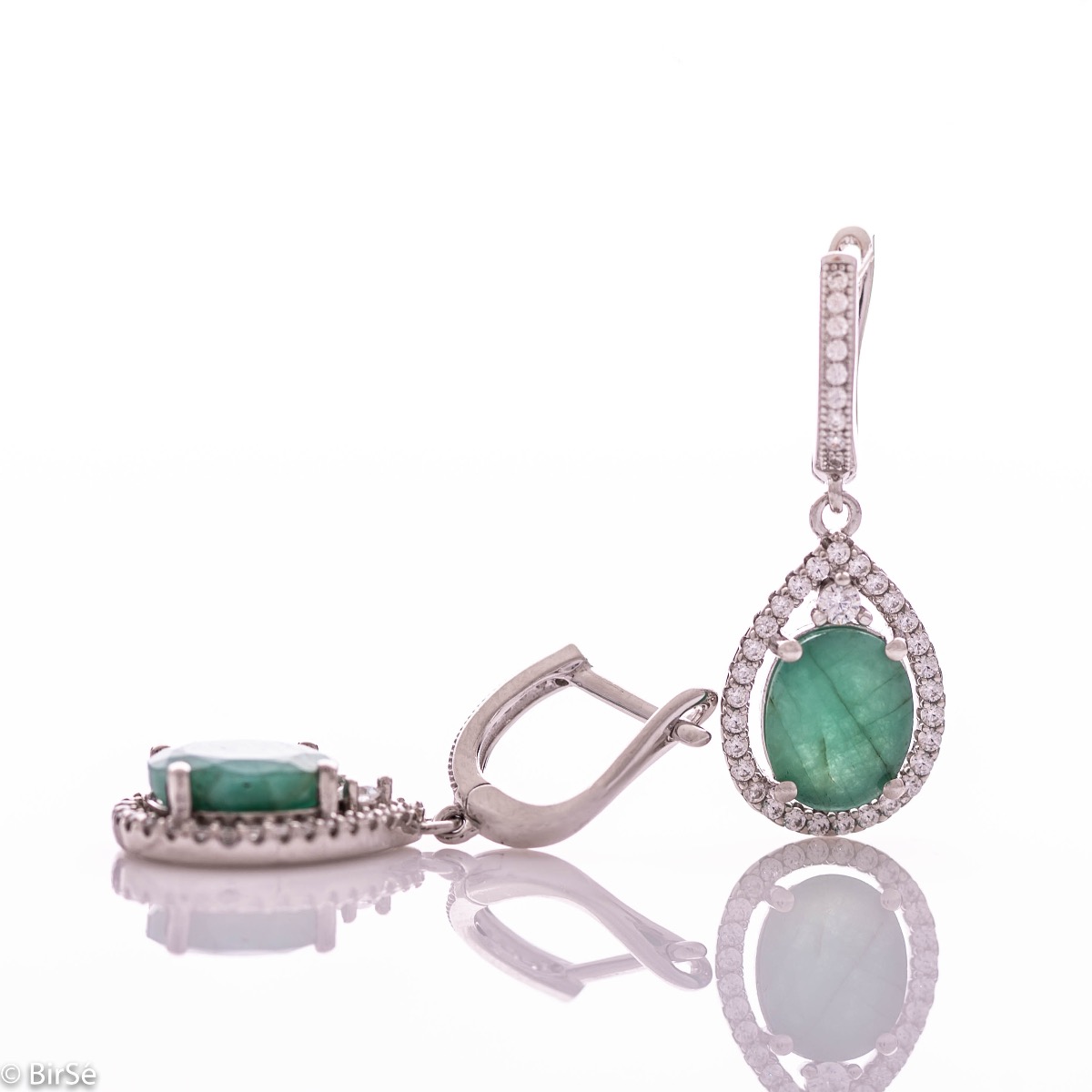 Elegant ladies' earrings with an English clasp and an impressive design combining delicate rhodium silver with a radiant natural emerald surrounded by sparkling zircons. They can be combined with a pendant and a ring of the same model.