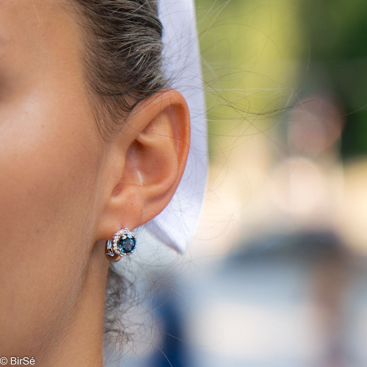 Magnificent earrings in delicate rhodium silver. A round shaped natural London topaz stone lies in the center surrounded by spectacular cubic zirconias.