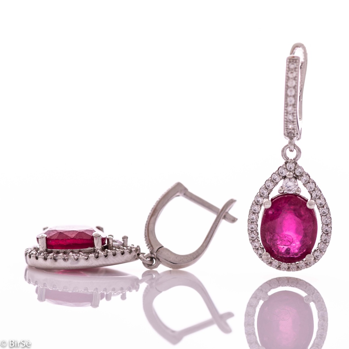 Exquisite ladies' earrings with English fastening and an impressive design combining delicate rhodium silver with a radiant natural ruby ​​surrounded by sparkling zircons. They can be combined with a pendant and a ring of the same model.