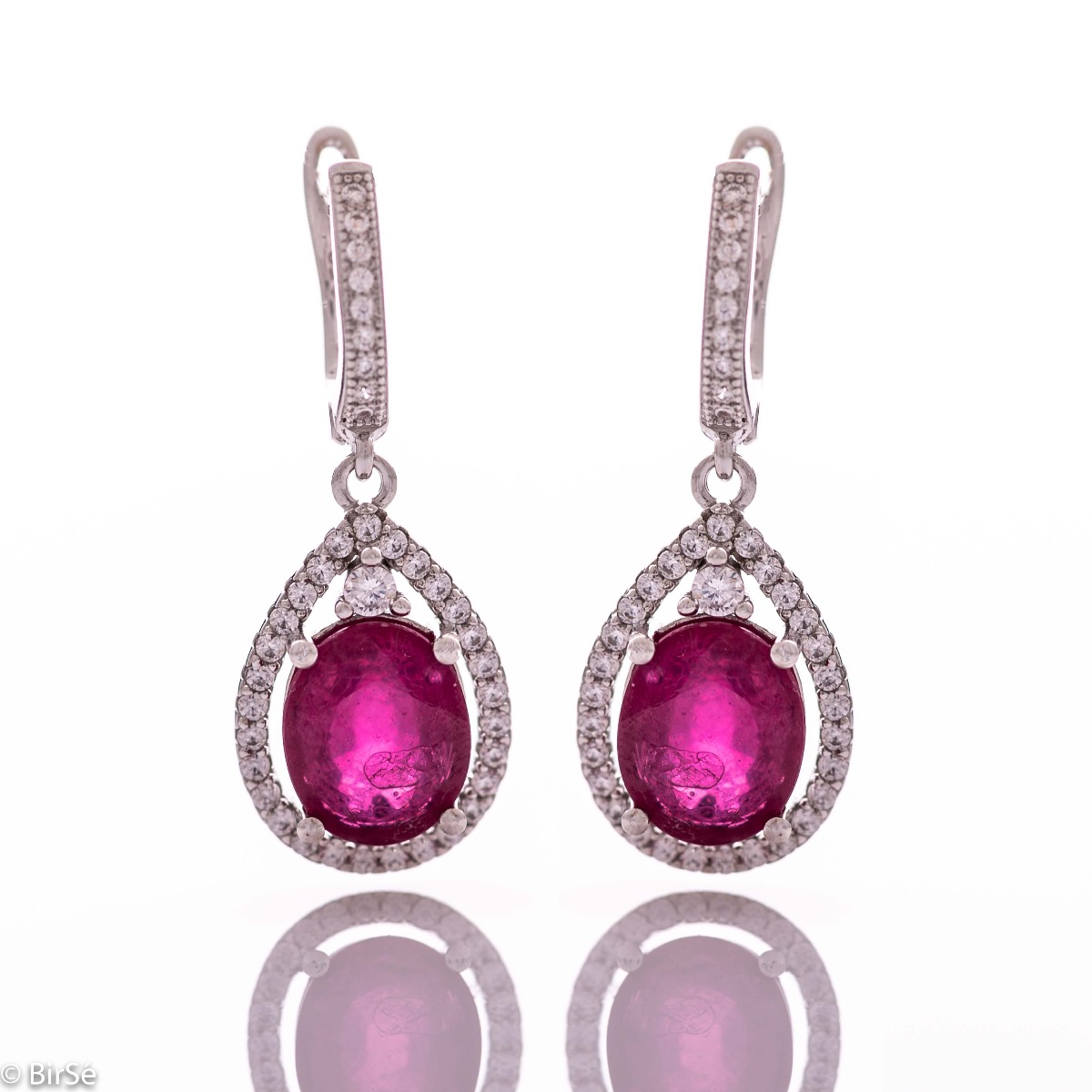 Exquisite ladies' earrings with English fastening and an impressive design combining delicate rhodium silver with a radiant natural ruby ​​surrounded by sparkling zircons. They can be combined with a pendant and a ring of the same model.