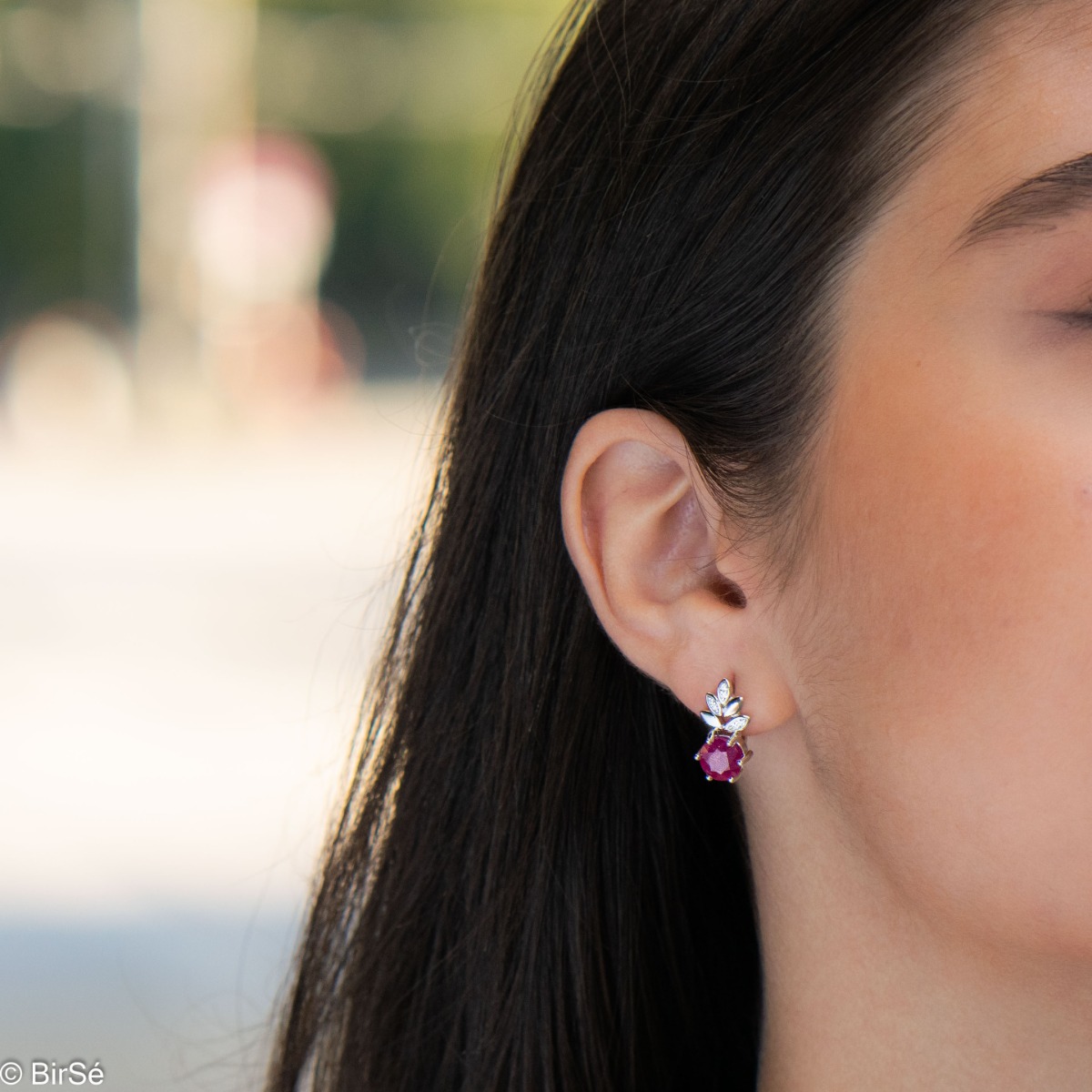 Delicate ladies' earrings with an English clasp and an exclusive design combining a radiant natural ruby ​​surrounded by cubic zirconia petals and made entirely of rhodium-plated silver. They can be combined with a pendant and a ring of the same model.