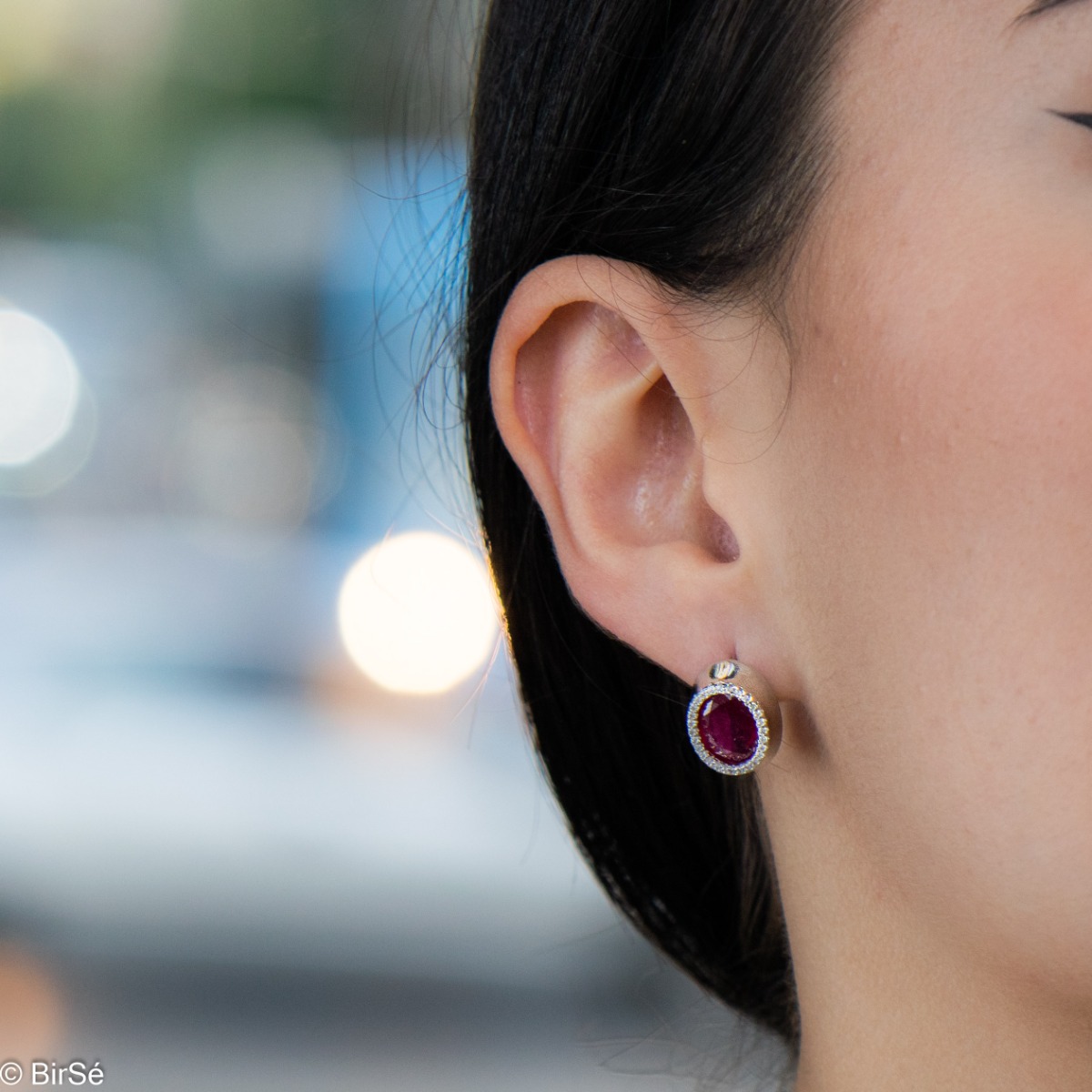 Elegant women's earrings with an English clasp and a classic design combining a radiant natural ruby ​​surrounded by sparkling zircons with delicate rhodium silver. They can be combined with a ring and pendant of the same model.