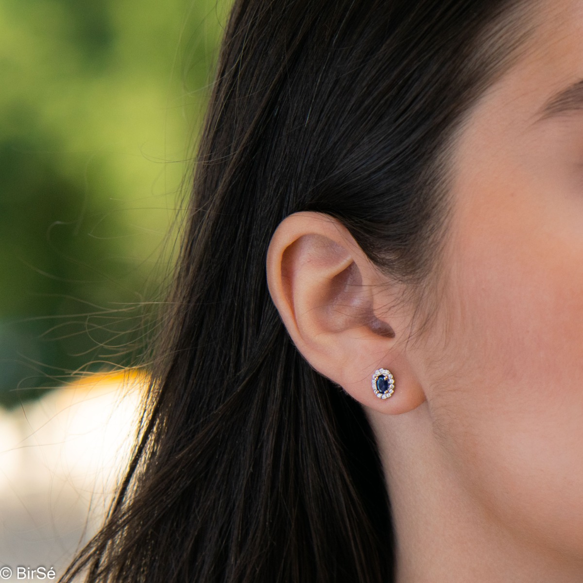 Stylish women's earrings with an elegantly shaped pattern of rhodium-plated silver and a natural sapphire stone, beautifully surrounded by dazzling zircons.