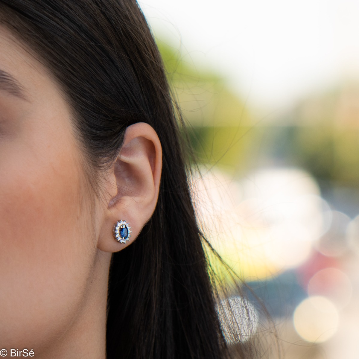 Delicate and radiant women's stud earrings with exquisite workmanship combining a unique natural sapphire, surrounded by sparkling zircons, with rhodium-plated silver. They can be combined with a ring, necklace and bracelet of the same model.