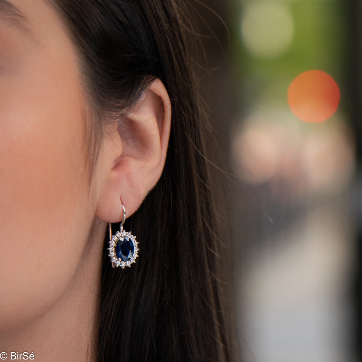 Exclusive women's earrings with exquisite workmanship combining delicate rhodium silver with a radiant natural sapphire surrounded by sparkling zircons.