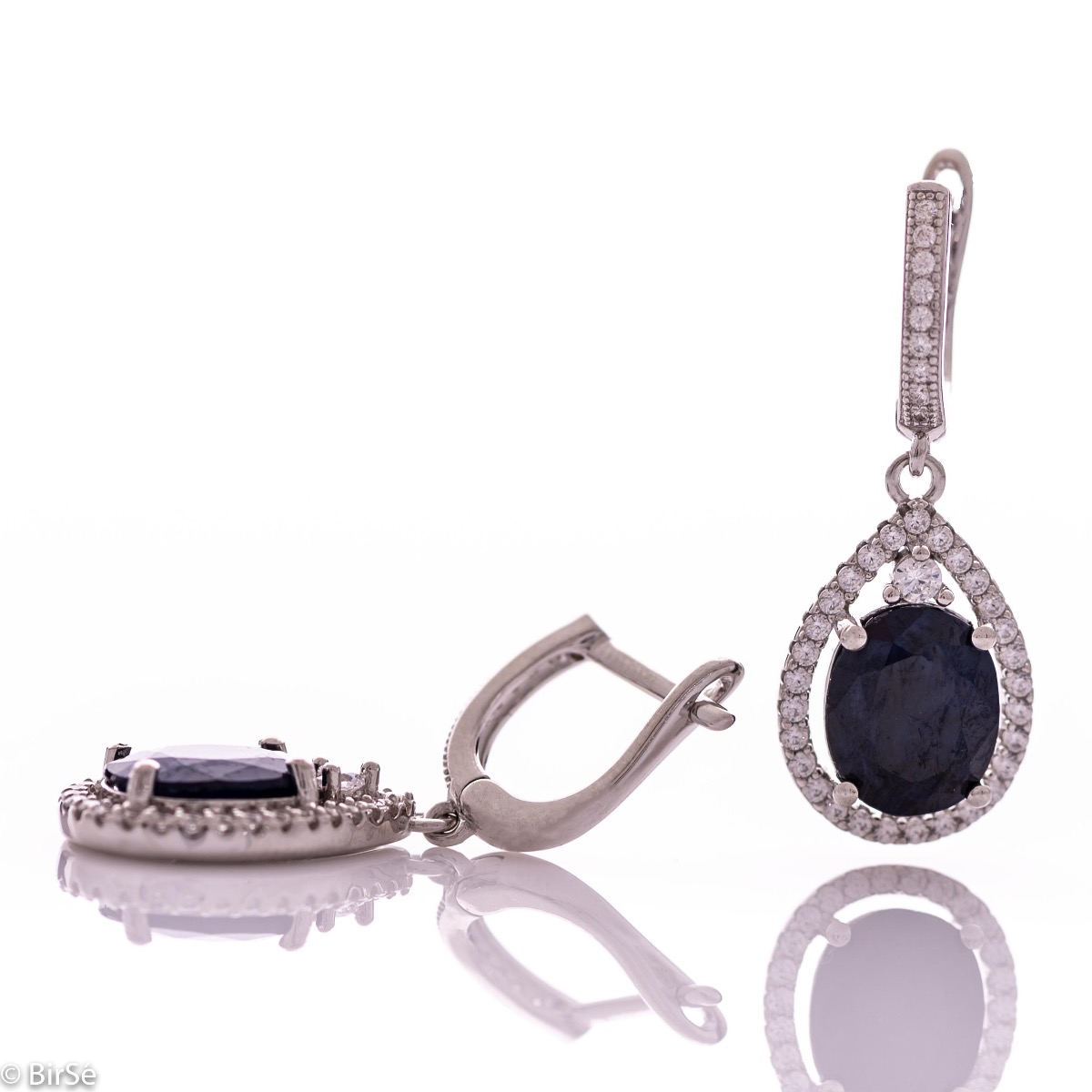 Exquisite ladies' earrings with an English clasp and an impressive design combining delicate rhodium-plated silver with a radiant natural sapphire surrounded by sparkling zircons. They can be combined with a pendant and a ring of the same model.