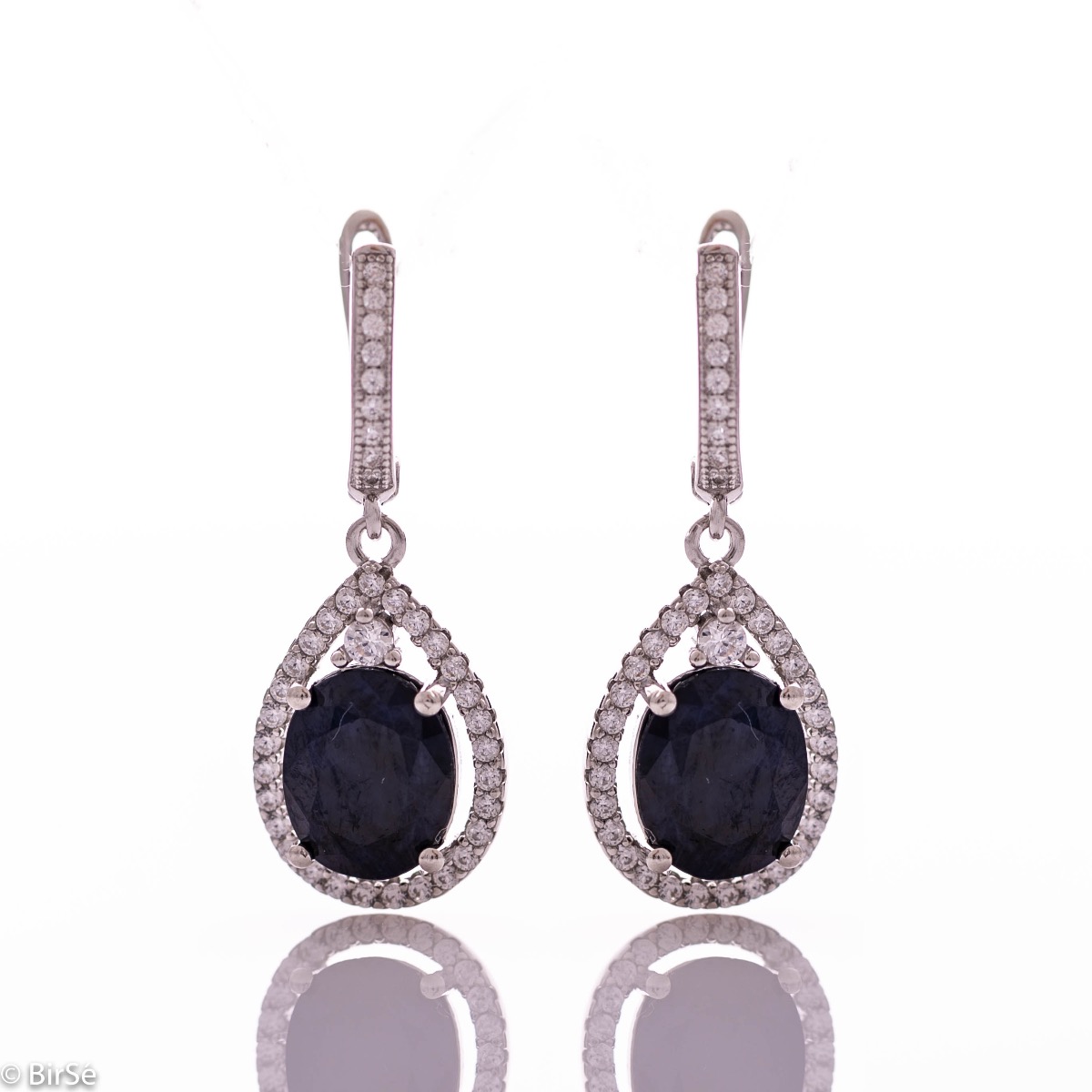 Exquisite ladies' earrings with an English clasp and an impressive design combining delicate rhodium-plated silver with a radiant natural sapphire surrounded by sparkling zircons. They can be combined with a pendant and a ring of the same model.