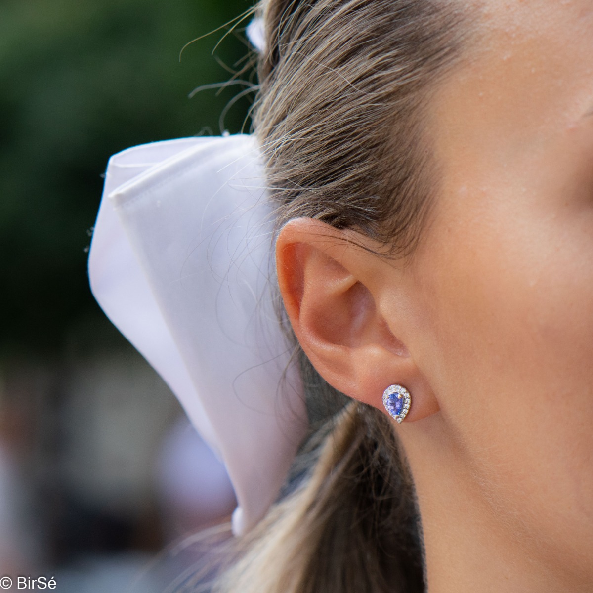 Elegant women's stud earrings with delicate drop-shaped natural tanzanite surrounded by sparkling zircons and exquisitely crafted in beautiful rhodium silver. In a charming ring, necklace and bracelet set.