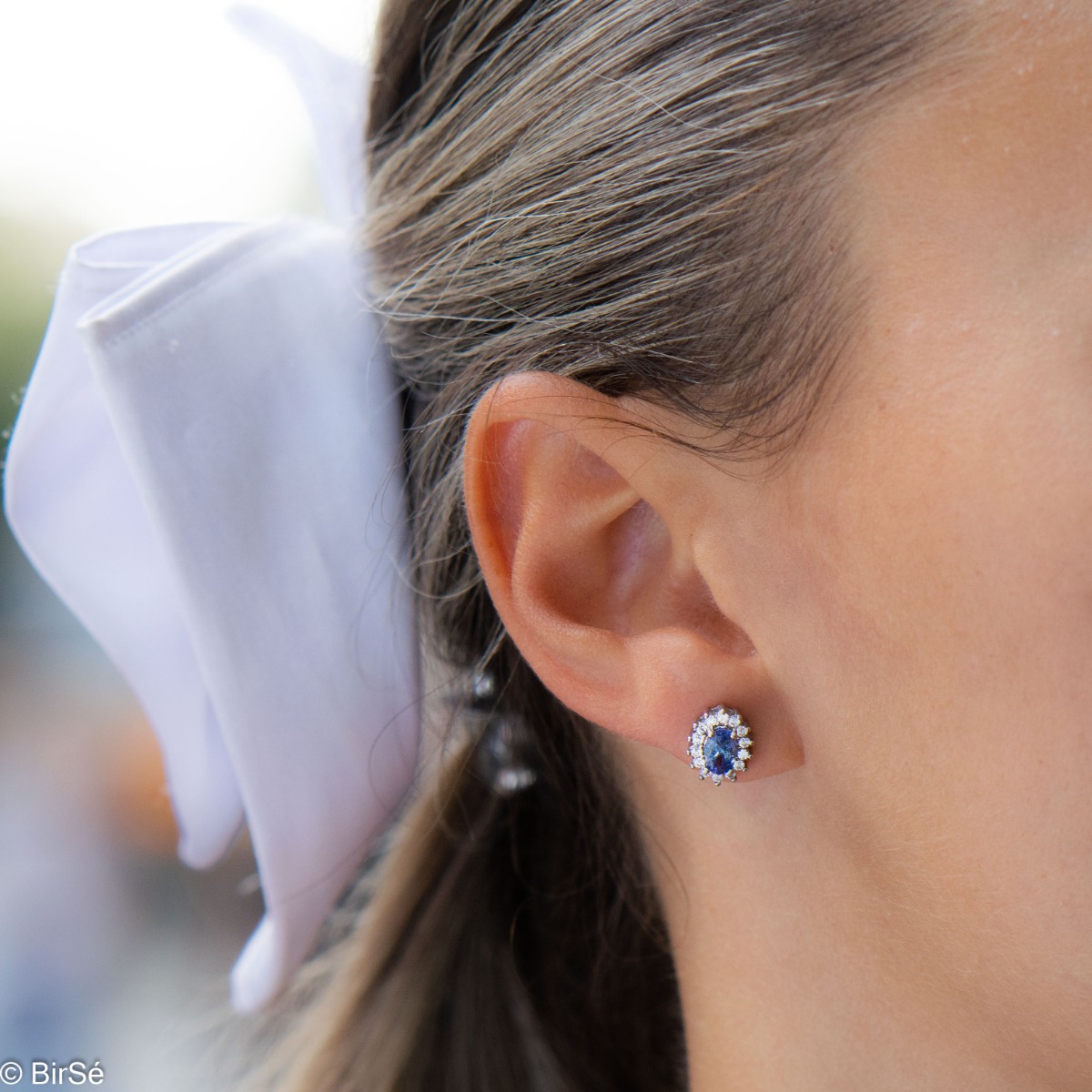 Delicate and radiant women's stud earrings with exquisite workmanship combining a unique natural tanzanite, surrounded by sparkling zircons, with rhodium-plated silver. They can be combined with a ring, necklace and bracelet of the same model.