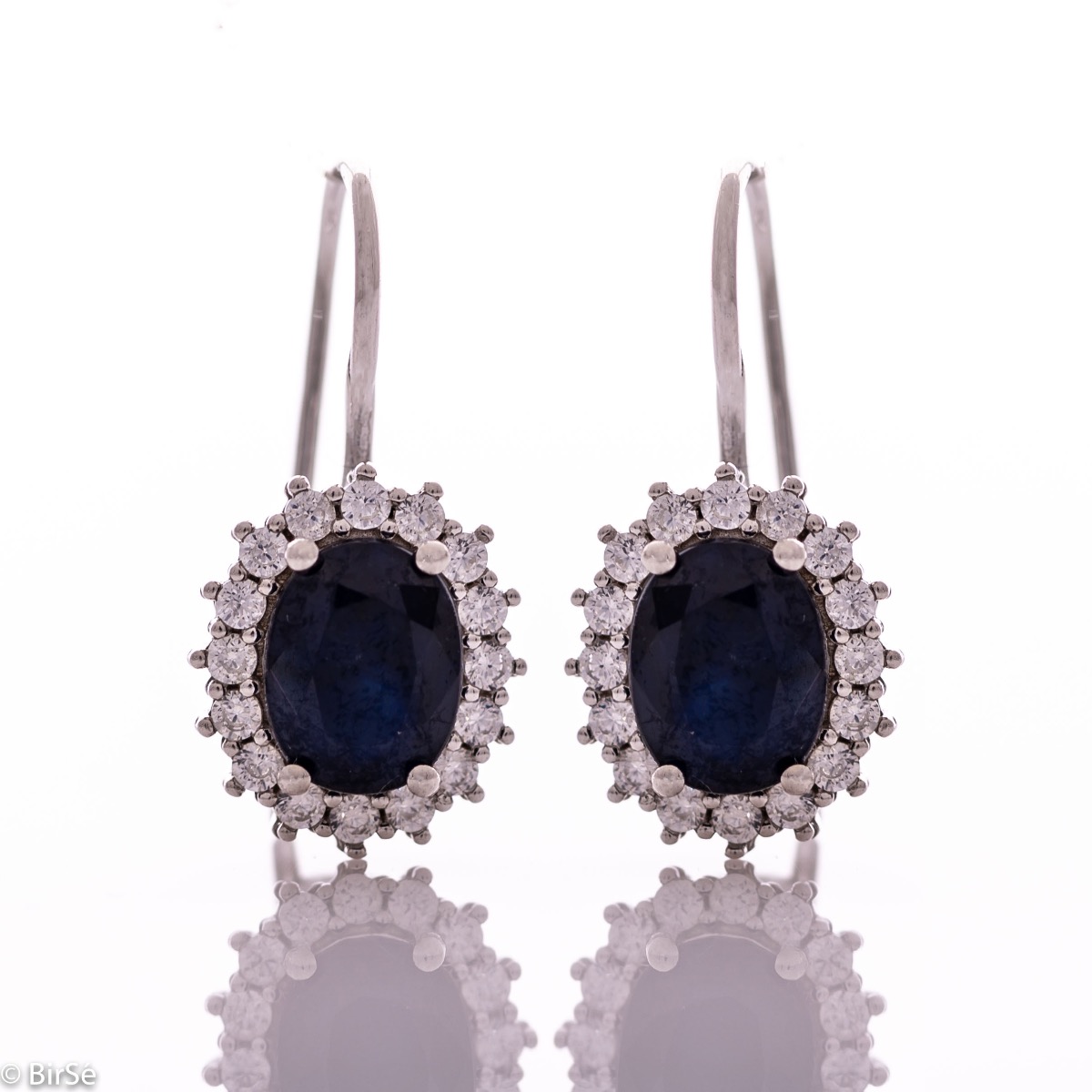 Exclusive women's earrings with exquisite workmanship combining delicate rhodium silver with a radiant natural sapphire surrounded by sparkling zircons.