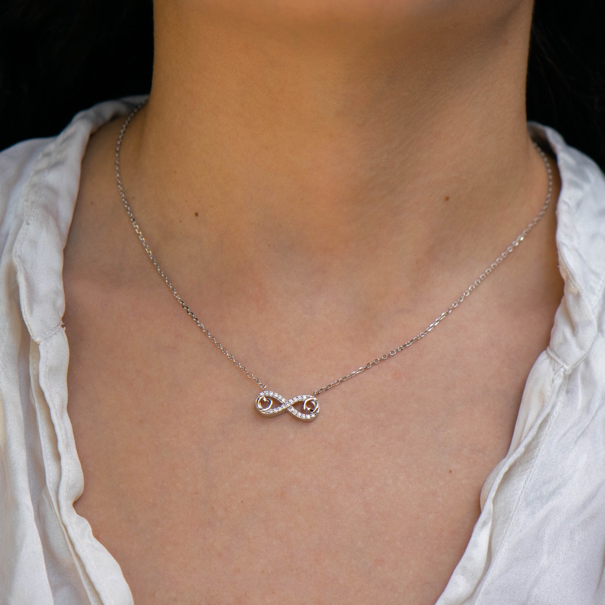 Delicate women's necklace with an exquisite infinity shape, intertwined with small hearts and precise craftsmanship entirely of rhodium-plated silver, complemented by sparkling zircons.