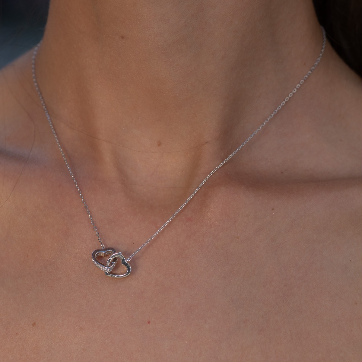 A rhodium-plated silver necklace with a delicate shape of intertwined hearts and a stylish design of side-mounted zircons.