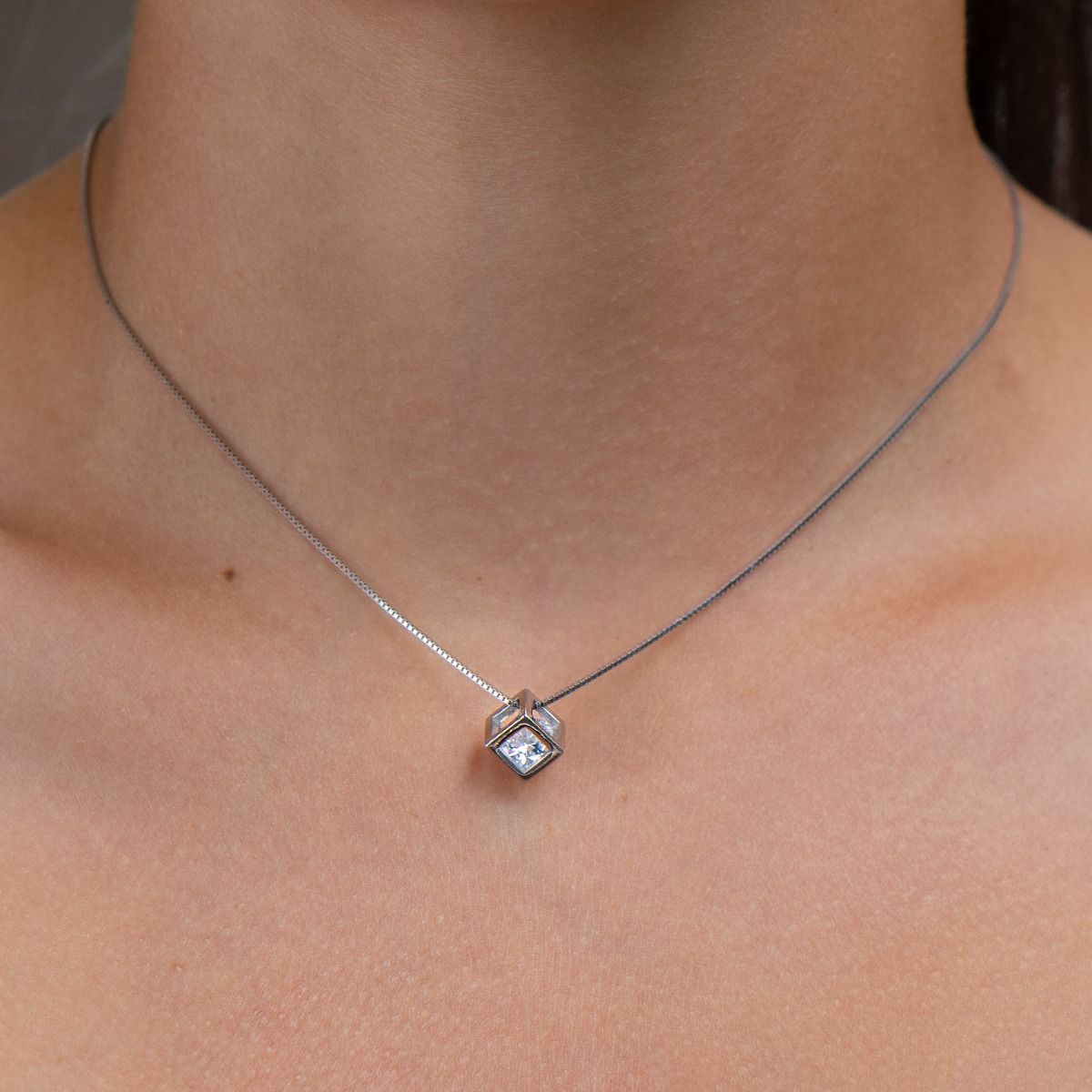 Elegant women's necklace with a modern design made of rhodium silver. The jewelry has a captivating craftsmanship - a delicate chain of classic Venetian braid, holds a cube-shaped element, elegantly enclosing a dazzling zircon.