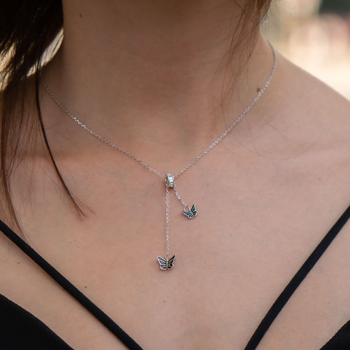 An exquisite women's necklace with precise craftsmanship and stylish design, combining rhodium-plated silver and a ring with sparkling fine zircons. Two delicate black enamel butterflies are mounted on a fine chain, threading through the ring and adding e