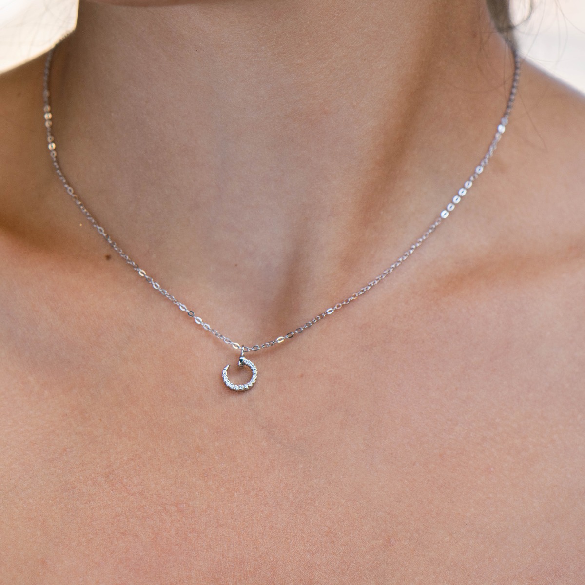 An exquisite silver necklace with a spectacular element of a small nail complemented by shiny zircons and made entirely of soft rhodium-plated silver.