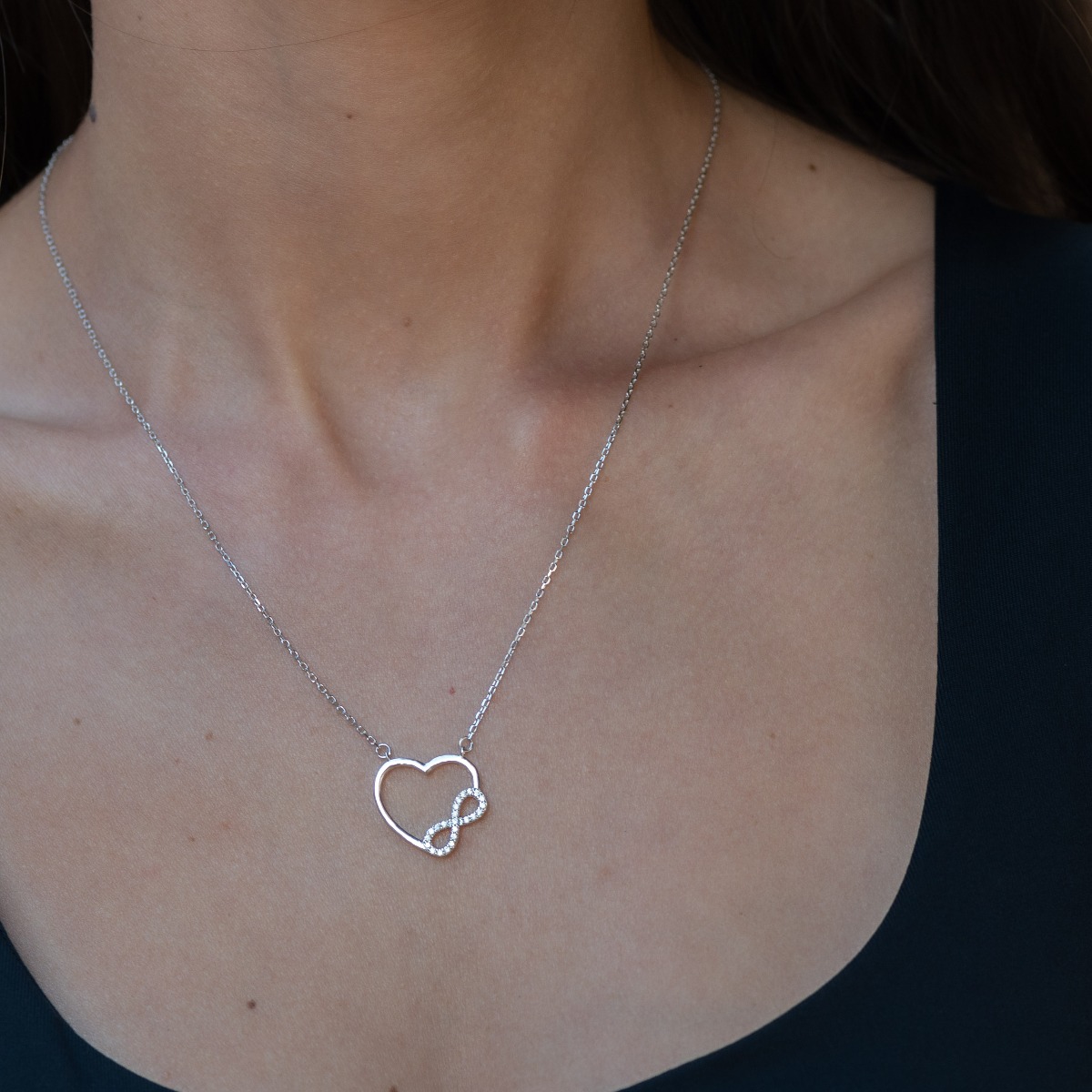 Extremely delicate silver necklace in the shape of a heart and infinity flowing into each other. Stylish compositional design of the elements and details from a fine combination of rhodium-plated silver with sparkling zircon stones.