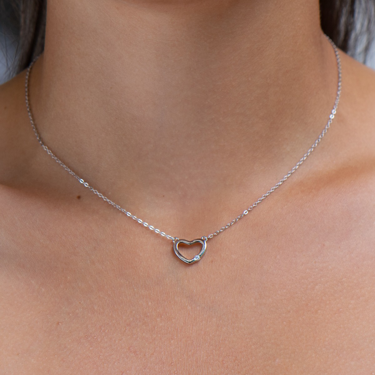 Delicate women's necklace with a charming design in rhodium silver. The piece features a delicate classic braided chain that holds a dainty heart with a dazzling cubic zirconia.