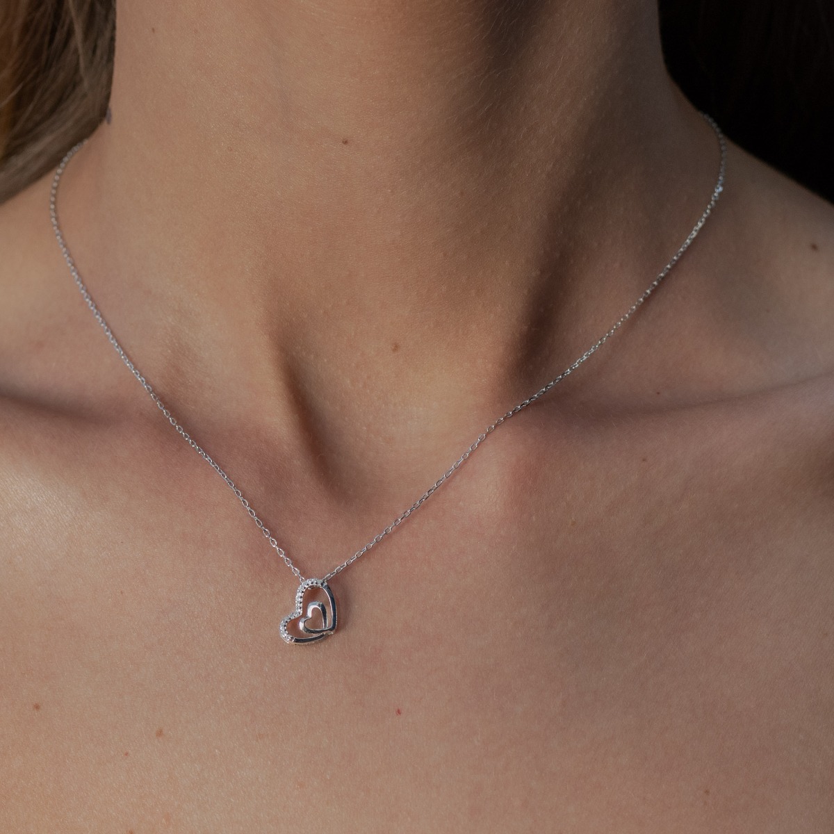 An exquisite women's necklace with two fine intertwined hearts, made entirely of soft rhodium-plated silver, complemented by the sparkle of white zircons.