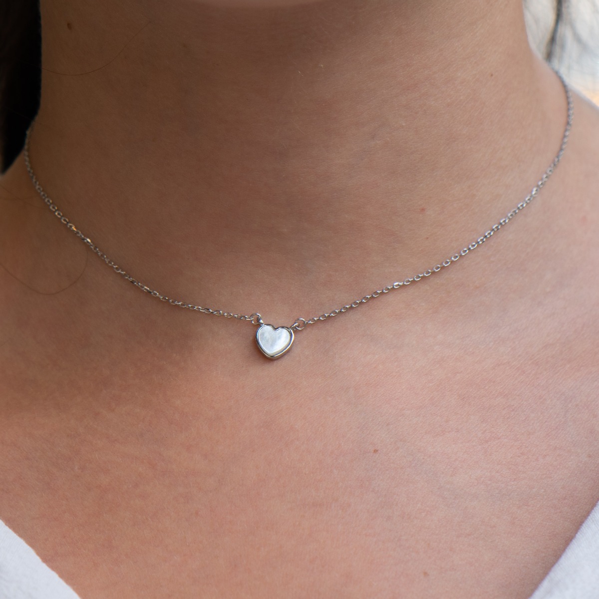 A stylish women's necklace, elegantly crafted from fine rhodium-plated silver as a fine chain holding a delicate mother-of-pearl heart. The jewelry is suitable for every lady's everyday life.