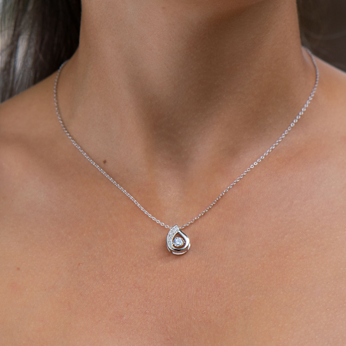 Elegant women's necklace with an exquisite design of rhodium-plated silver with a teardrop shape. The jewel is of unique craftsmanship - a delicate zircon charmingly twitching among other, smaller stones.